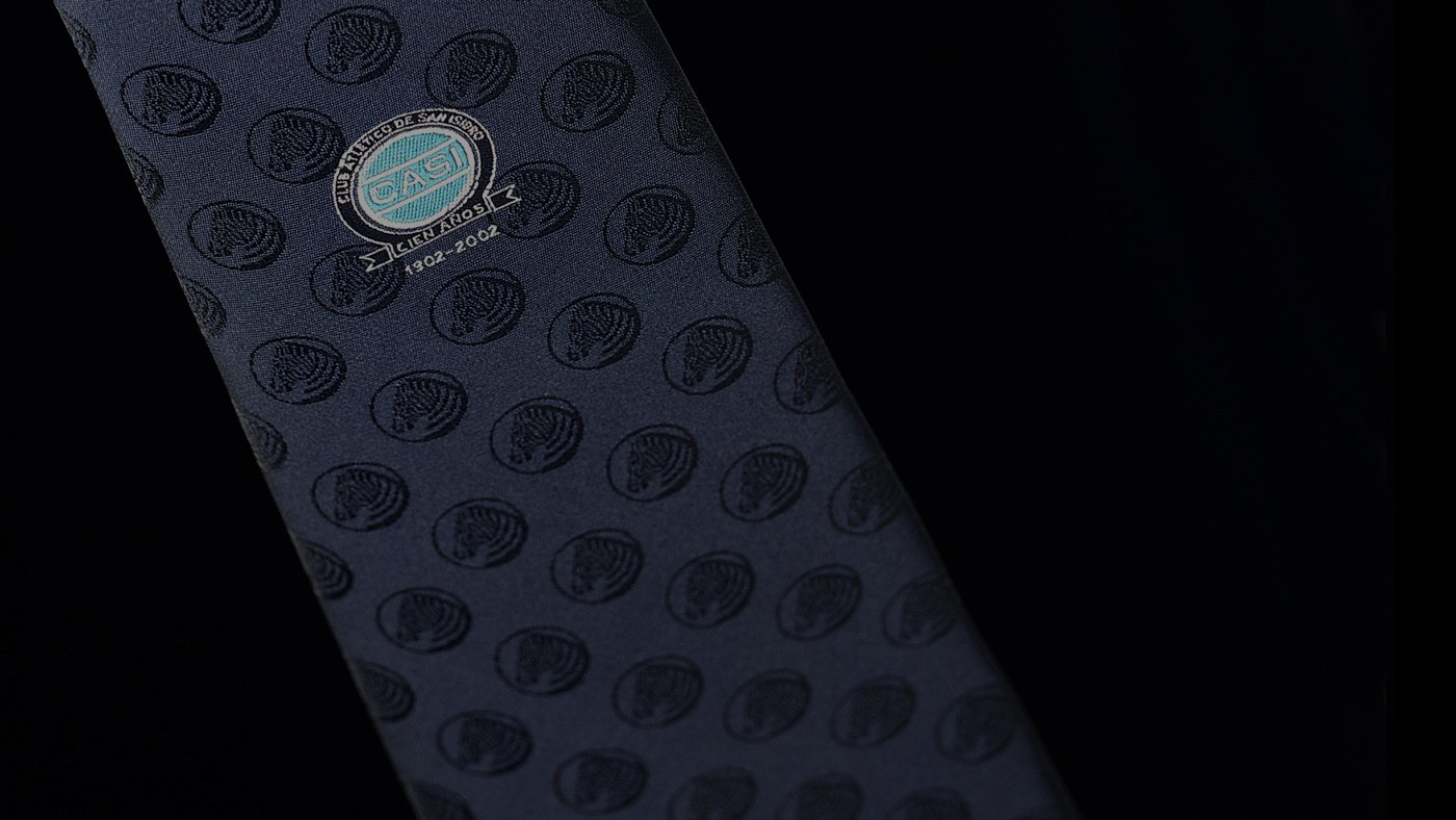 Dark tie with embossed circle patterns, featuring a small circular logo that reads "CACI" and dates "2004-2005", set against a black background.