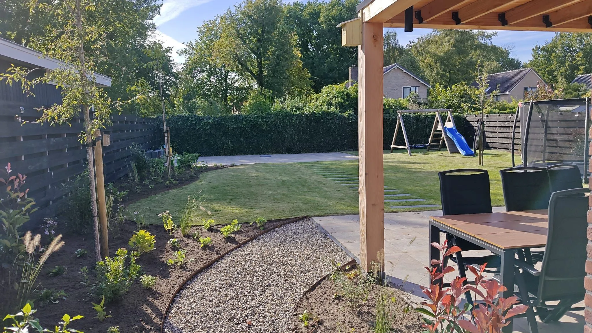 Kindvriendelijke tuin met grasveld, schommel, trampoline, bestrating en nieuw aangeplante borders bij vrijstaande nieuwbouwwoning.
