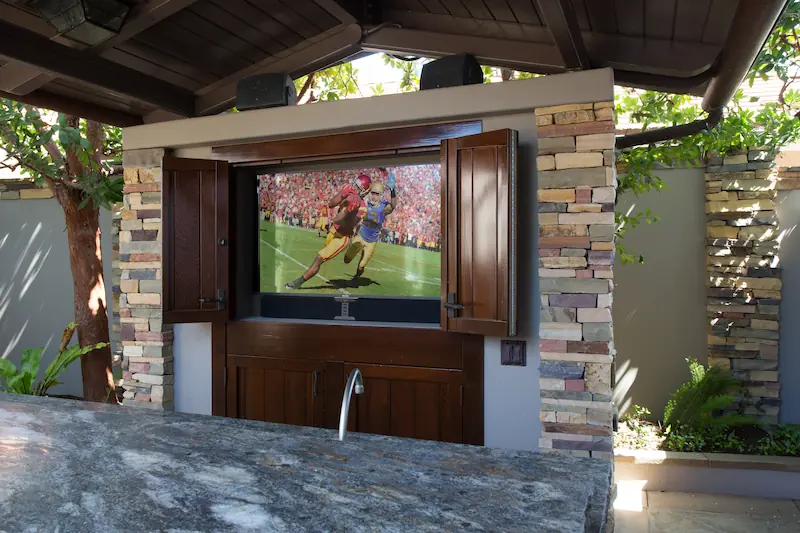 Opened entertainment cabinet with custom dark stained wood doors underneath a covered patio area from the Big Canyon Remodel project. Photo by Chris Darnall.