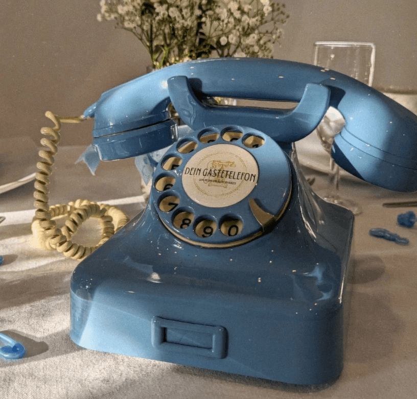 Pastellblaues Gästetelefon Ruby auf einem Tisch mit Blumendeko