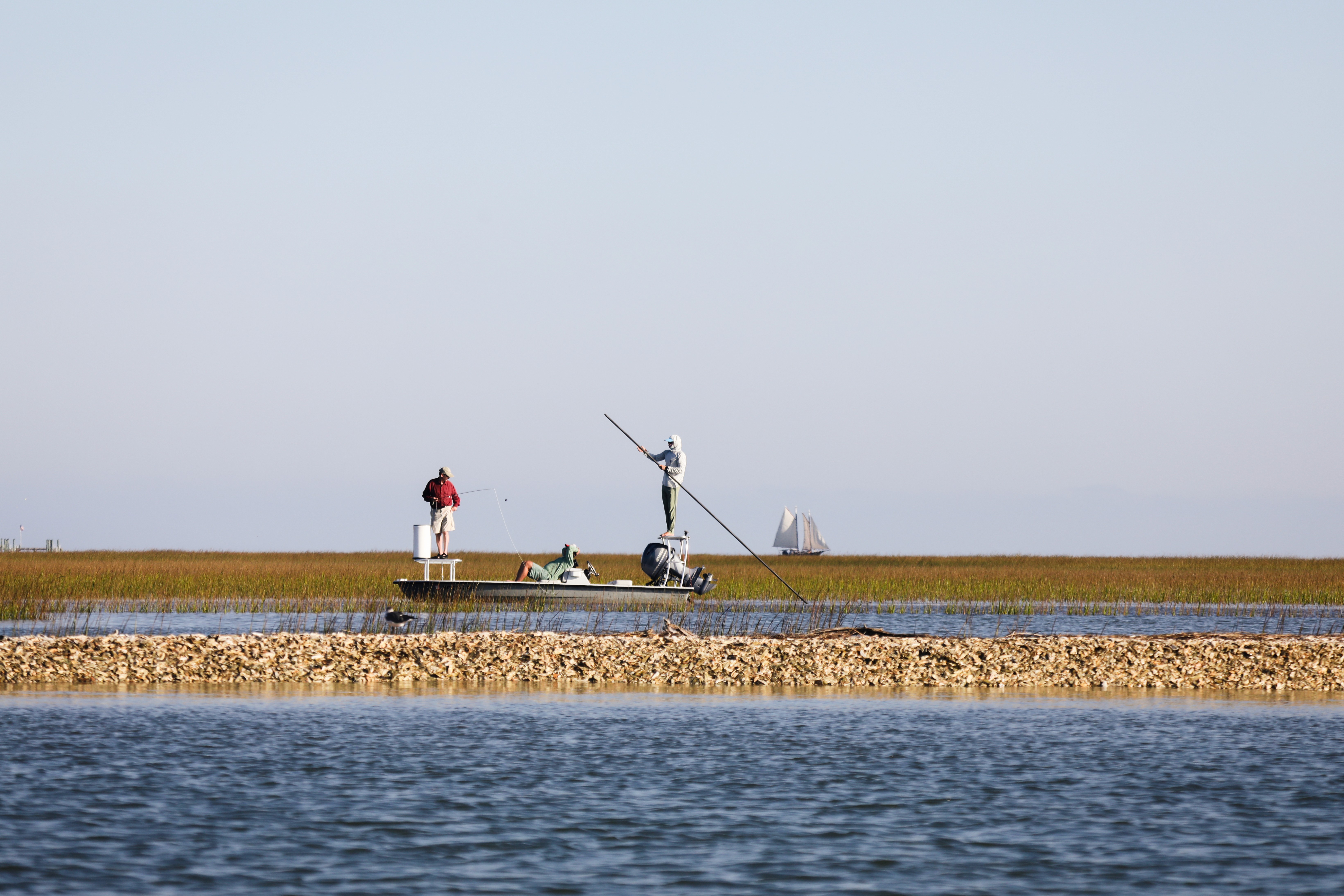 Two people fishing from a small boat in shallow coastal waters.
