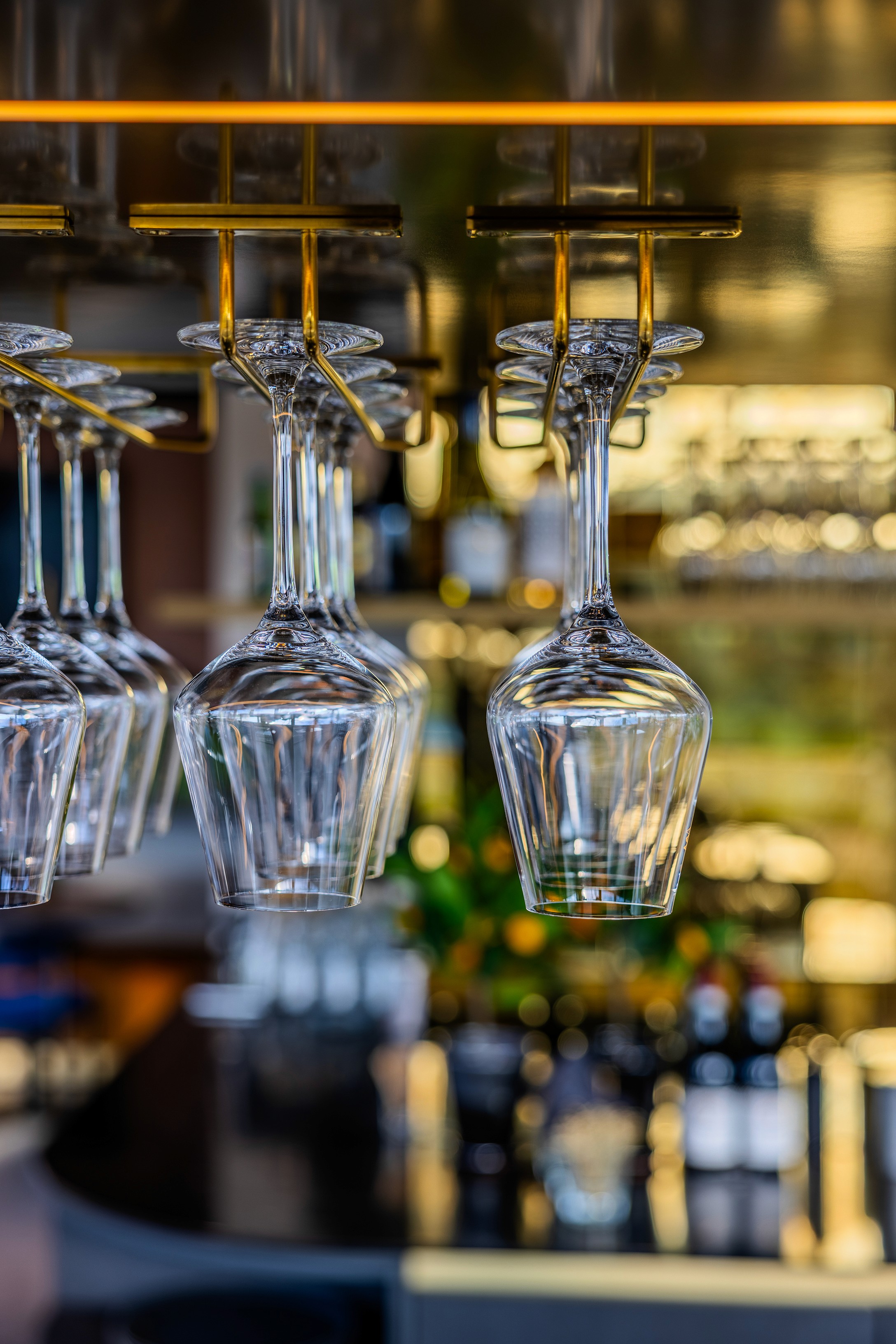 Detailopname van opgehangen wijnglazen boven de bar in AFAS DotNL, met flessen drank in de achtergrond en gouden kastelementen – interieurfotografie DSN Workspace Solutions