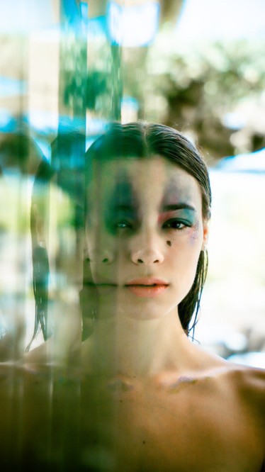 Vibrant digital illustration of a cat with blue eyes, featuring splashes of multicolored paint in yellow, blue, and pink on a dark background, showcasing a creative and artistic style.