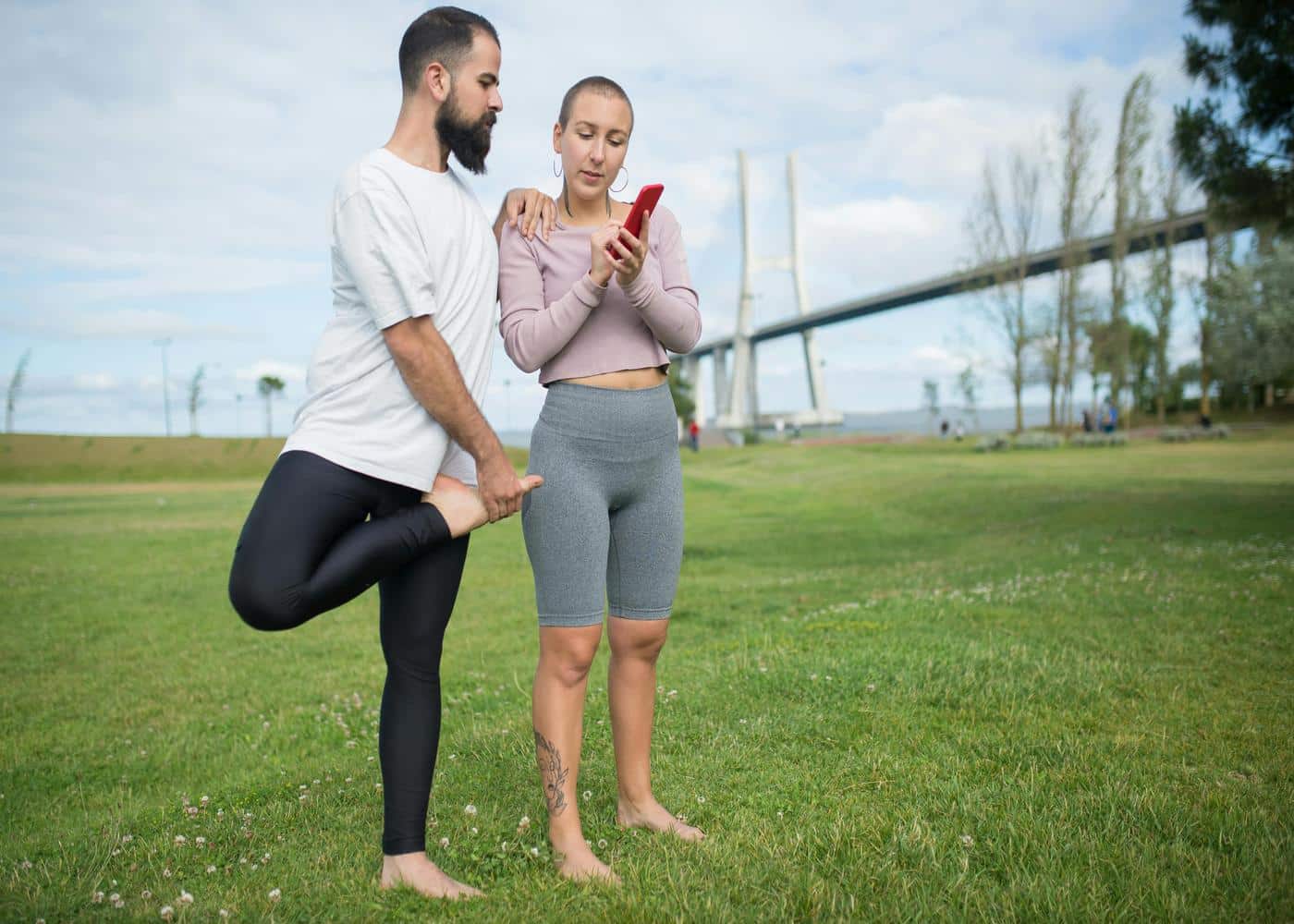 Couple outdoors looking at smart phone while man stretches leg in front of him