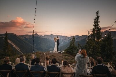 Guests watch the newlyweds dance beneath string lights with mountains spanning the horizon.