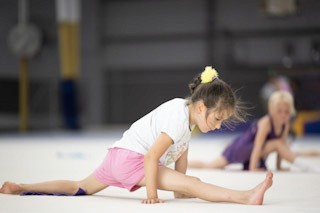 Two girls practicing their split at a preschool gymnastics class.