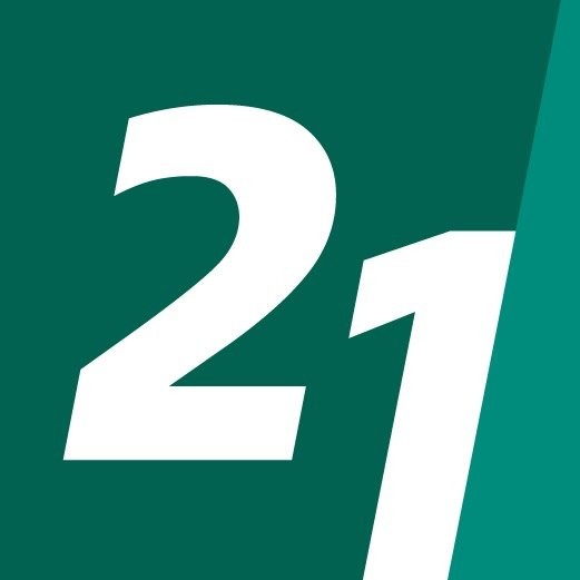 Young person with wavy hair poses confidently in sunlight against a modern building backdrop. Wears a black blazer and silver necklace, conveying elegance.