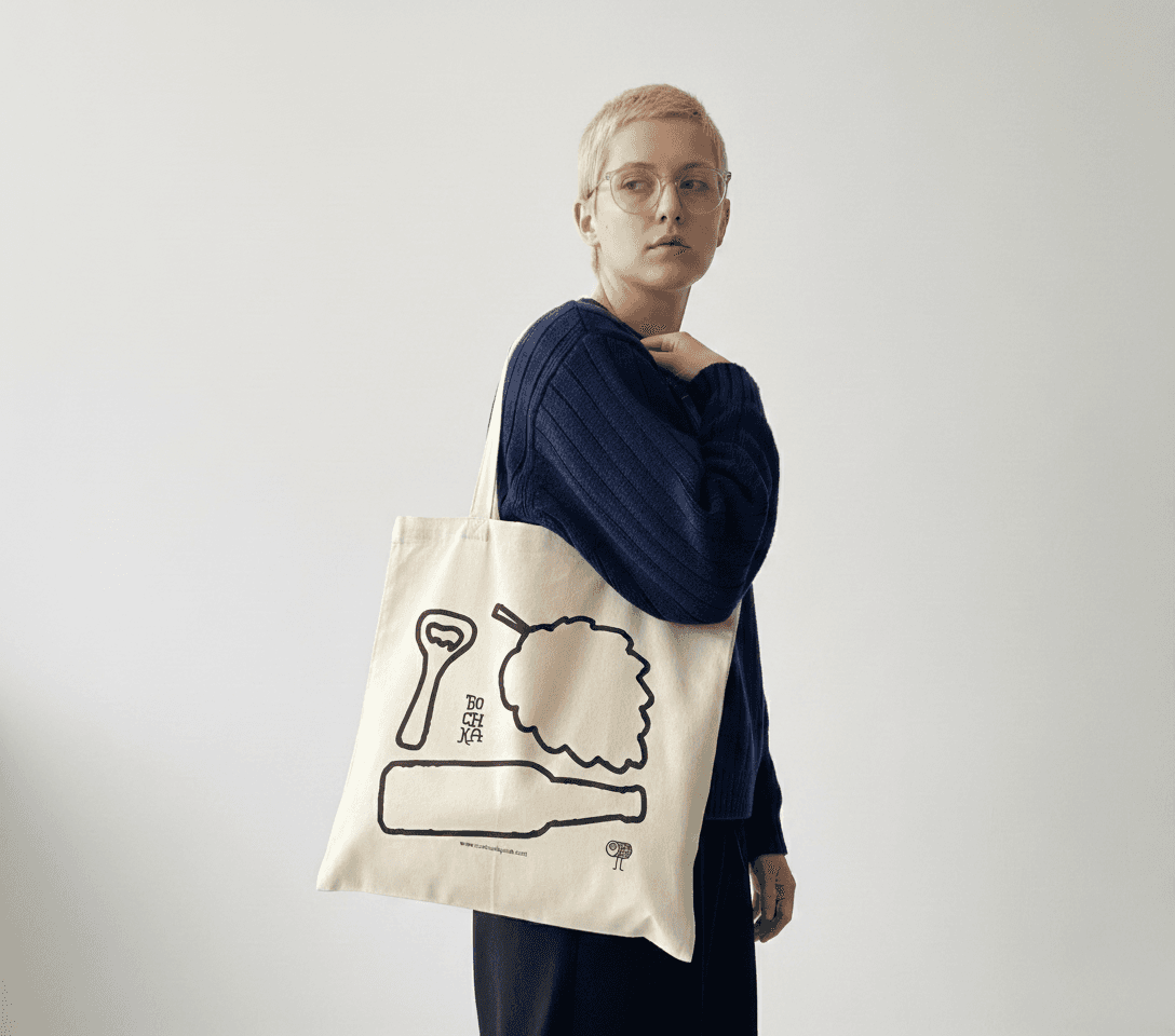 Young she/her wearing a branded totebag, with illustration on it. a Hoppy plant, a beer bottle and a bottle opener outline,