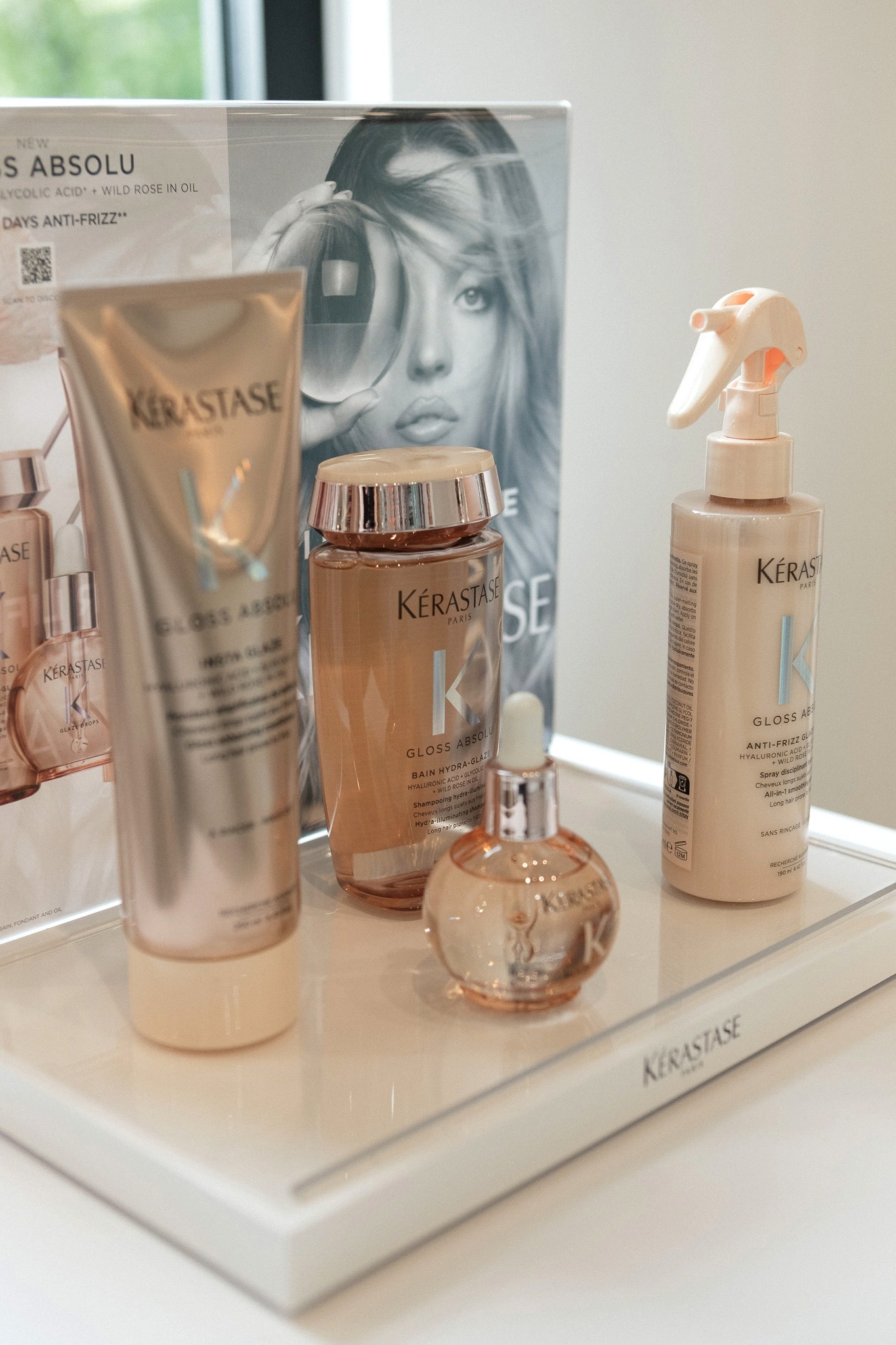 Smiling young woman with long hair standing against a dark green background, holding a finger to her chin.