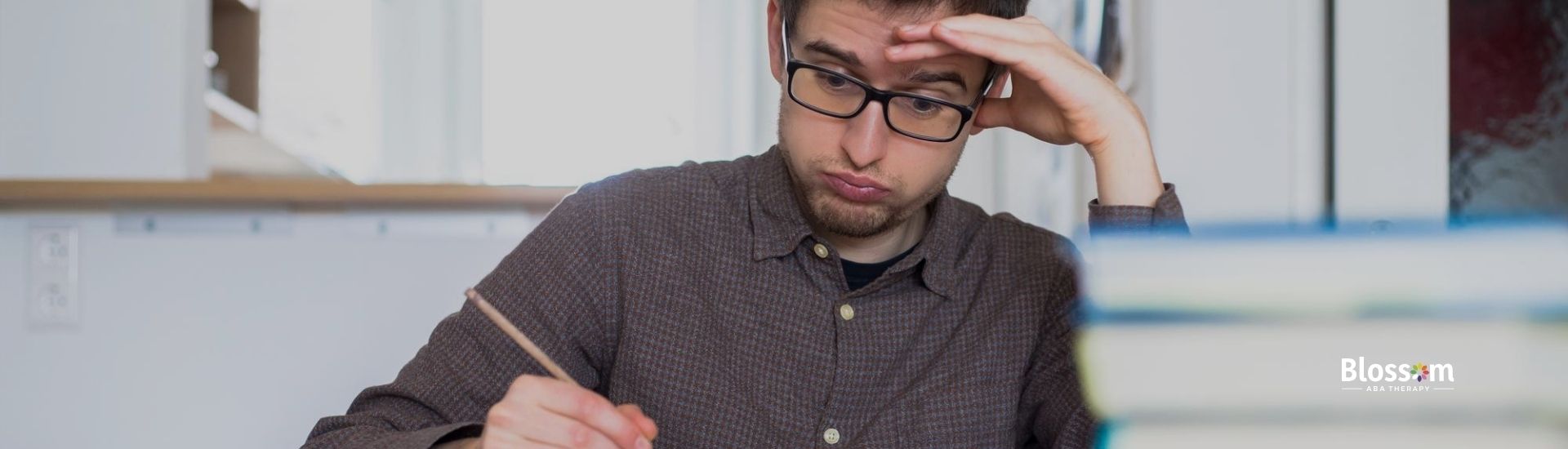 A man wearing glasses looks stressed while studying with an open book.