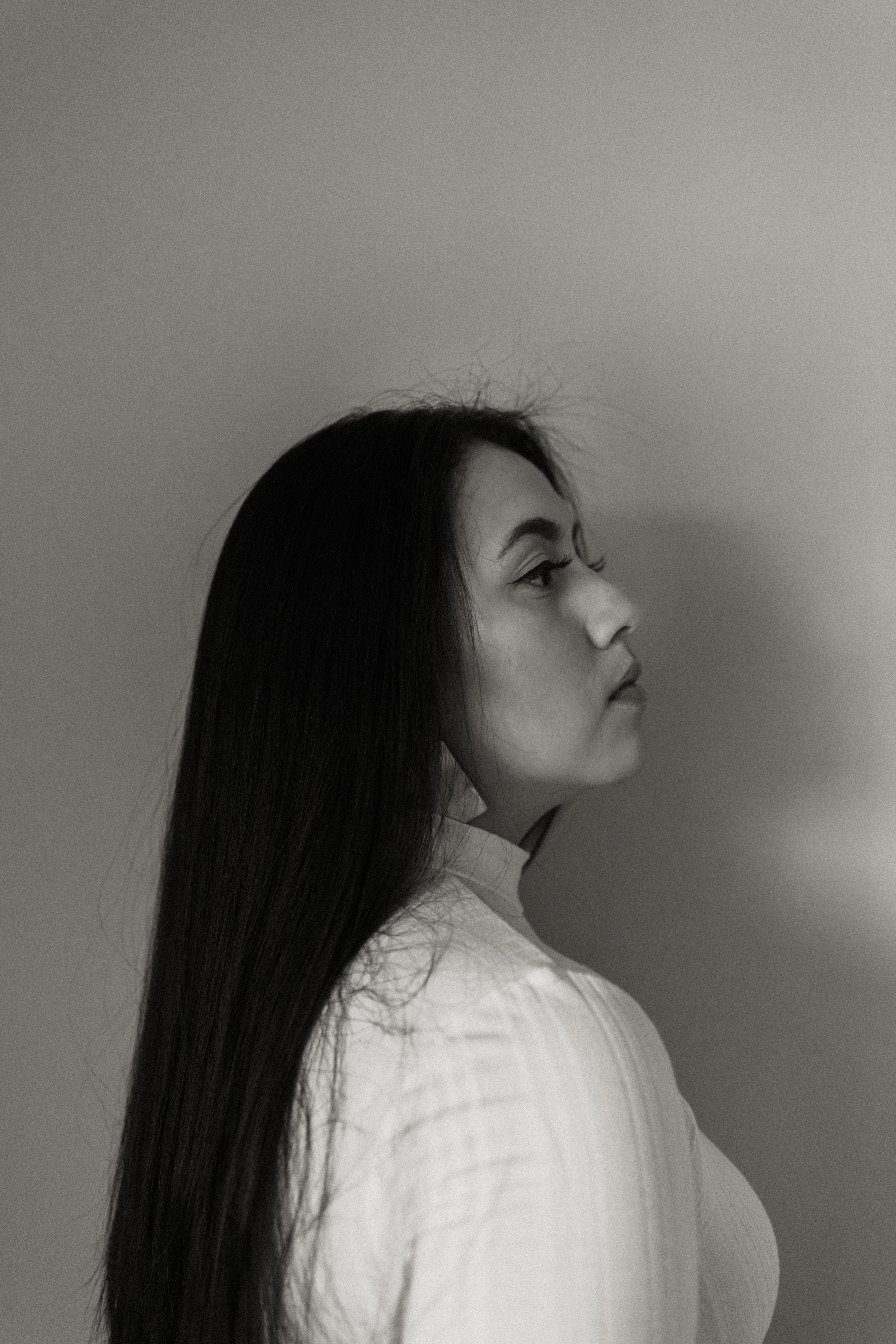 A thoughtful young person with dark hair gazes to the side, captured in soft black and white lighting.