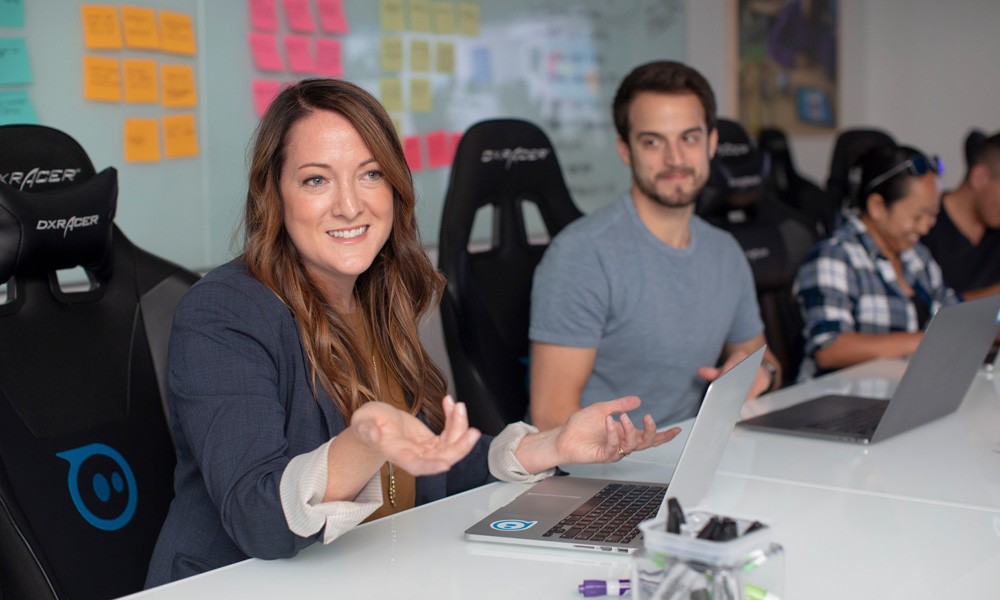 A team sitting around a table listening to one of their colleagues discussing a workshop. 