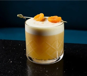 A frothy, bright orange cocktail on a sparkling black countertop.