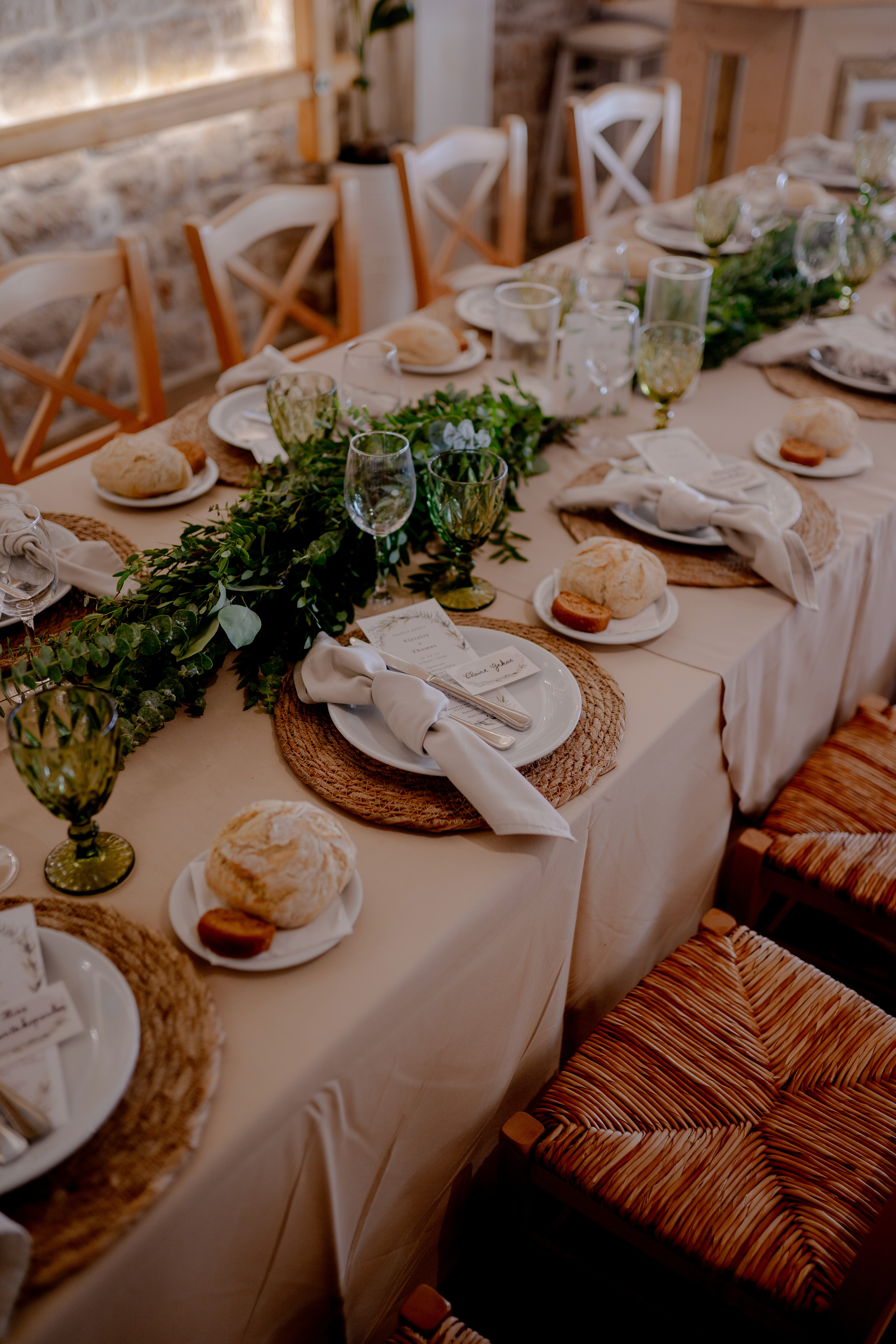 Μακρύ μοναστηριακό τραπέζι γάμου με εντυπωσιακή πράσινη γιρλάντα από ευκάλυπτο και ρουστίκ λεπτομέρειες