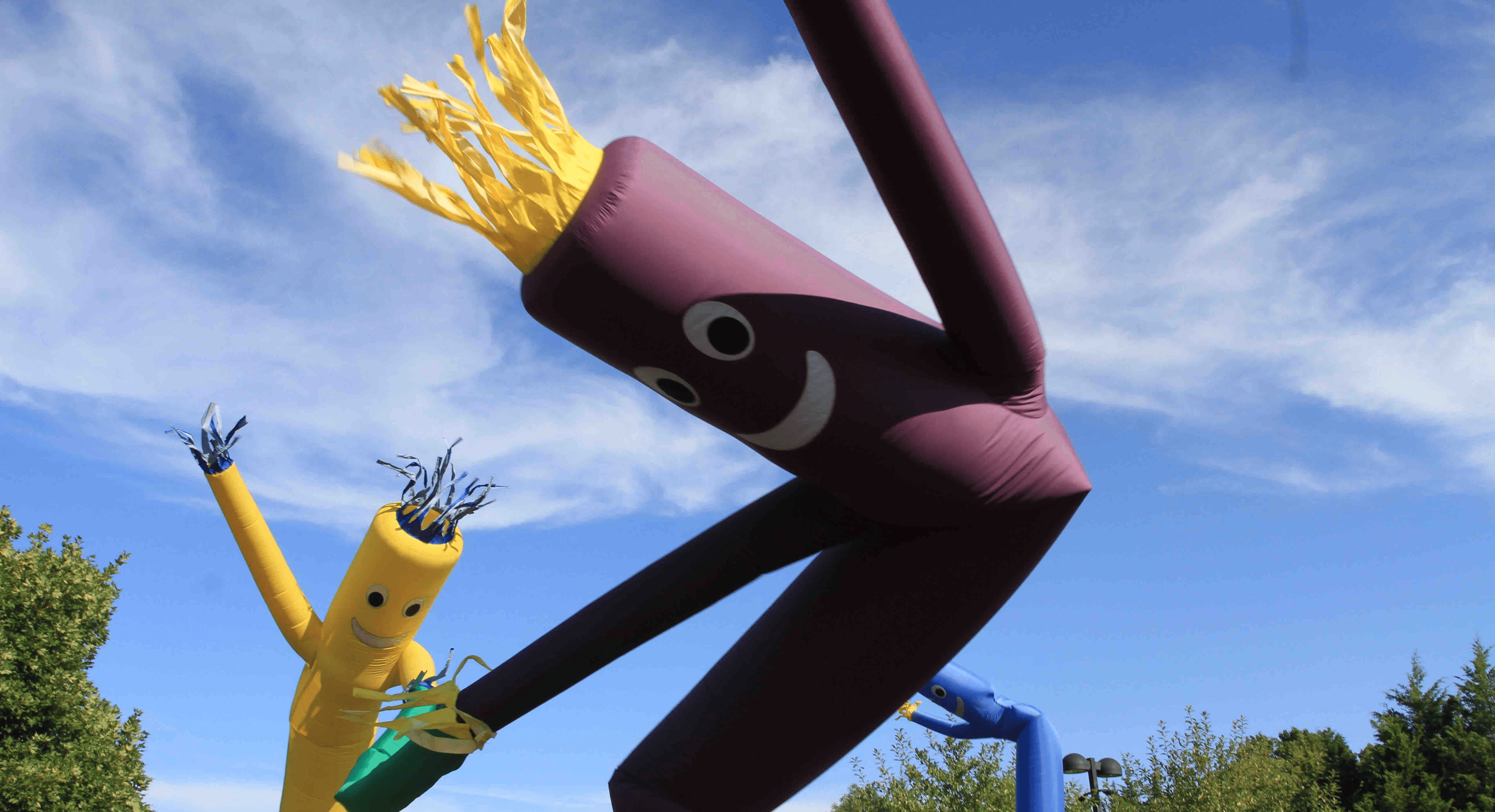 Colorful inflatable tube men dance in the wind against a clear blue sky.