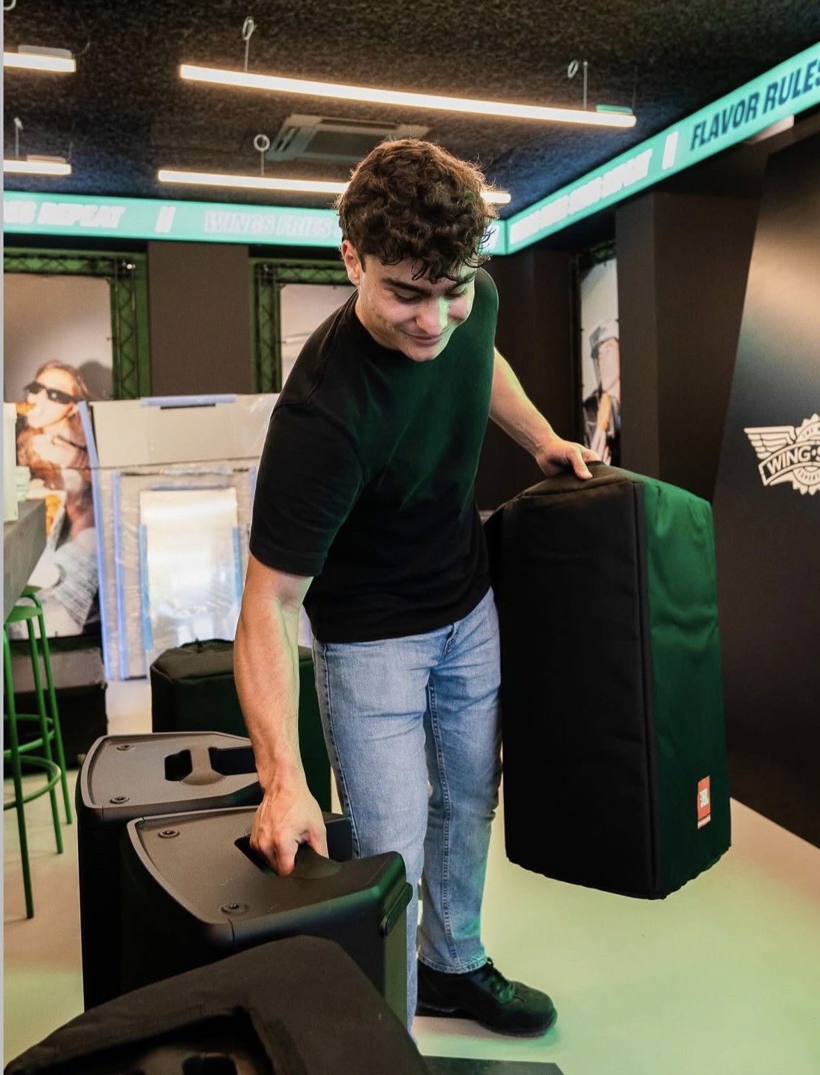 A smiling man with short hair stands with arms crossed, wearing a dark shirt against a neutral background.
