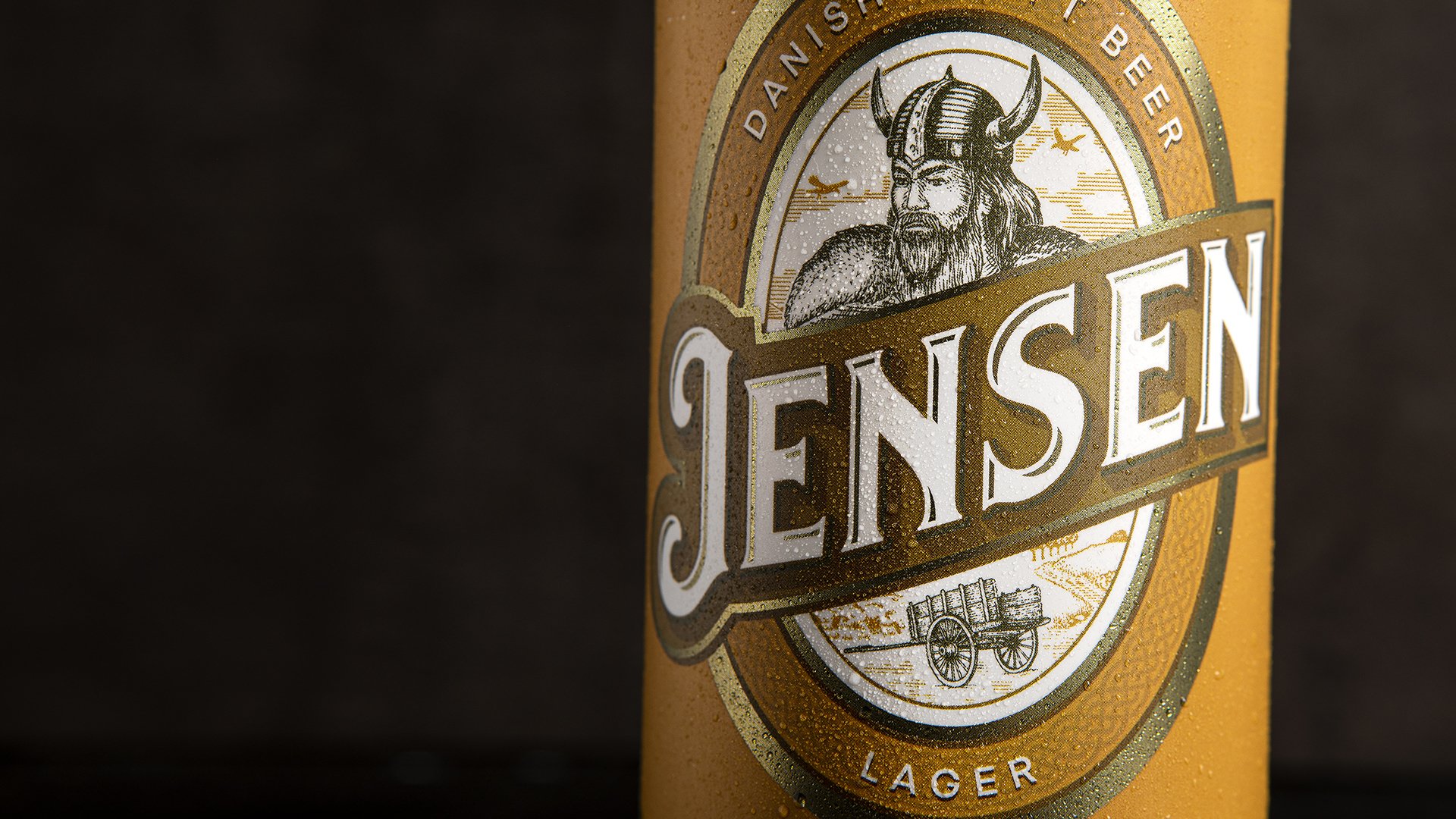 Close-up of a Jensen beer can with a Viking graphic. The can has a golden hue and is labeled "Danish Craft Beer" and "Lager" on a dark background.
