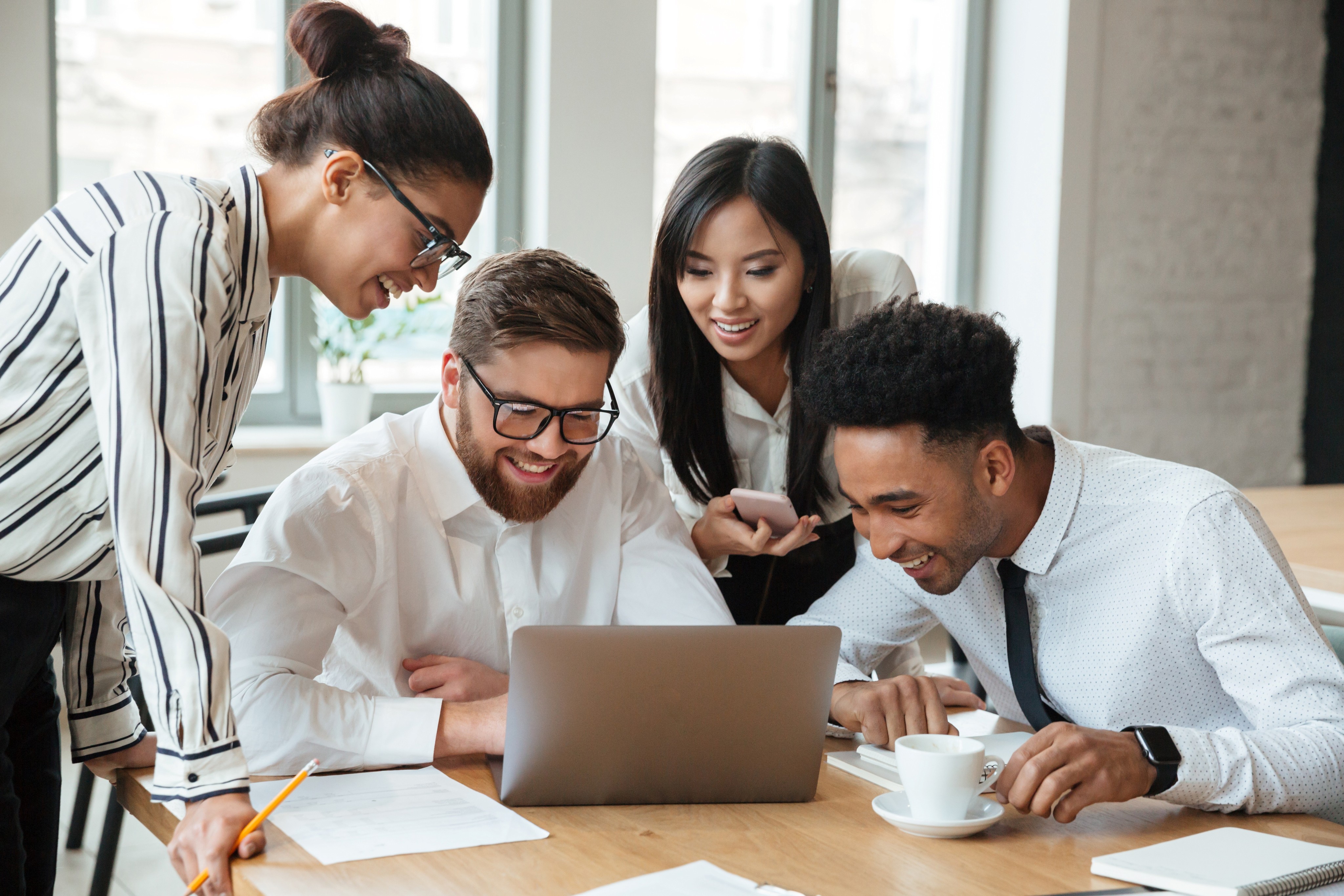 Four colleagues gather around a laptop in a modern workspace, collaborating effortlessly using smart workgroups, secure video conferencing, and enterprise-grade communication tools.