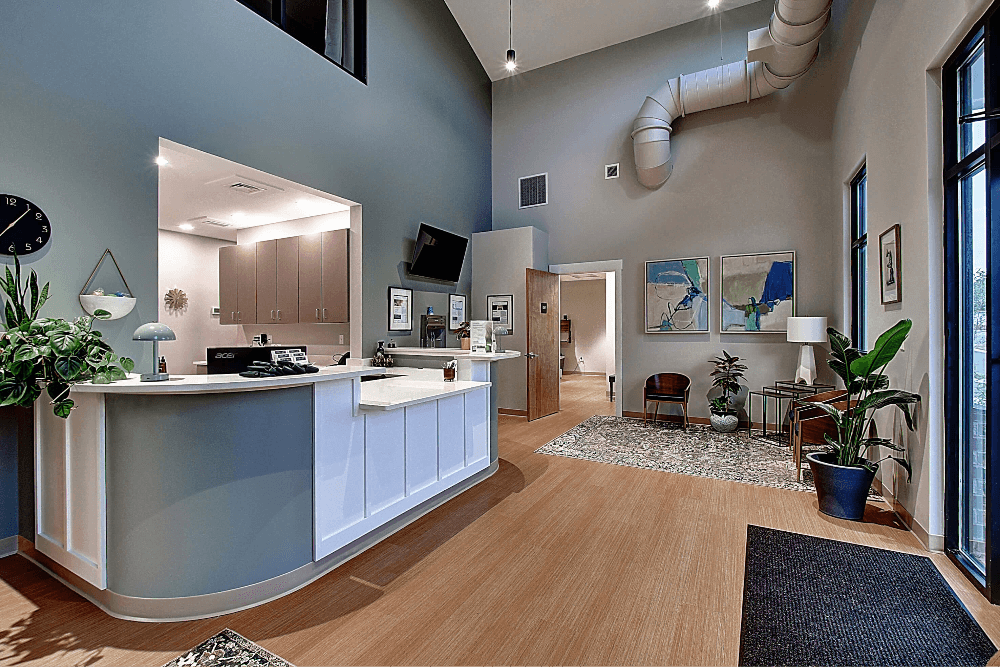 Bright, modern reception area with a white desk, wooden floors, and plants in a spacious, inviting setting.