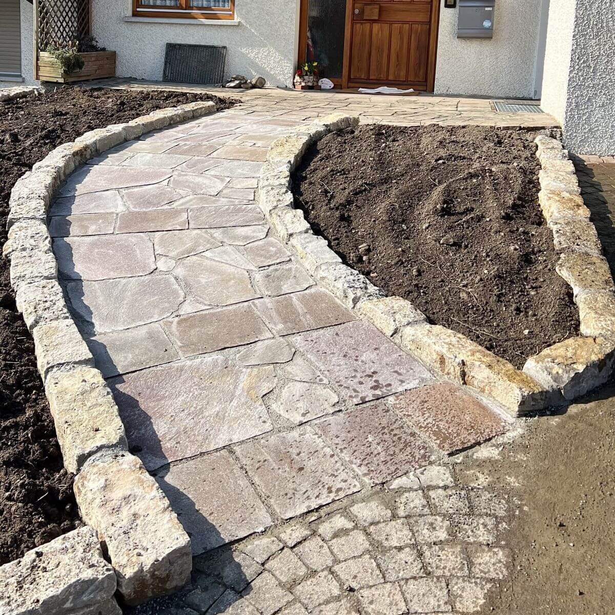 Geschwungener Gartenweg aus Natursteinplatten, eingefasst mit Würzburger-Muschelkalk..