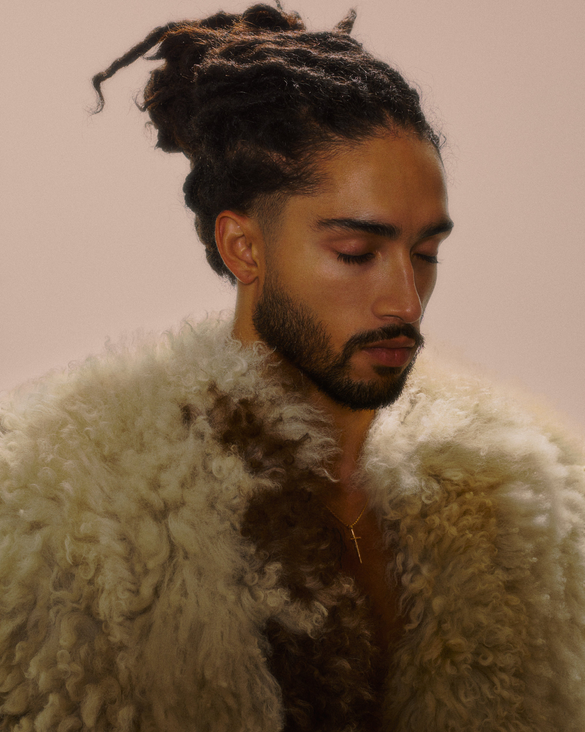 A man in a shearling coat, eyes downcast, shot in warm neutral tones.