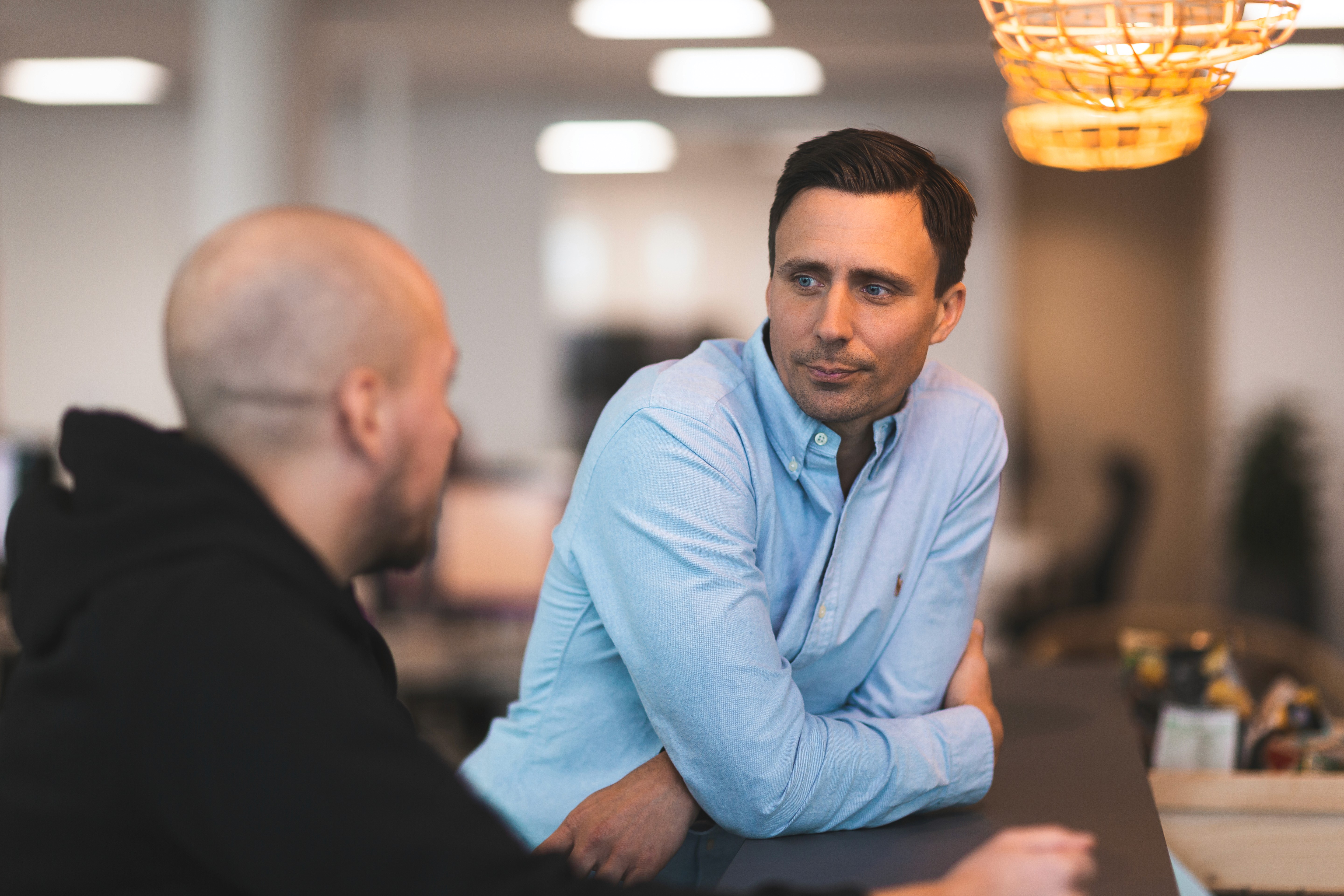 Two men staning by a bar at an office talking to eachother