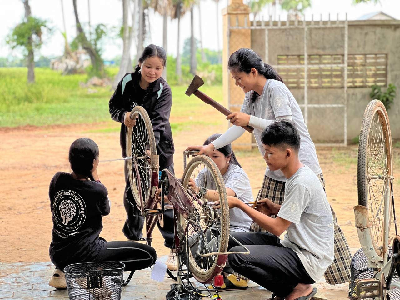 A group of students learns how to repair a bicycle in rural Cambodia