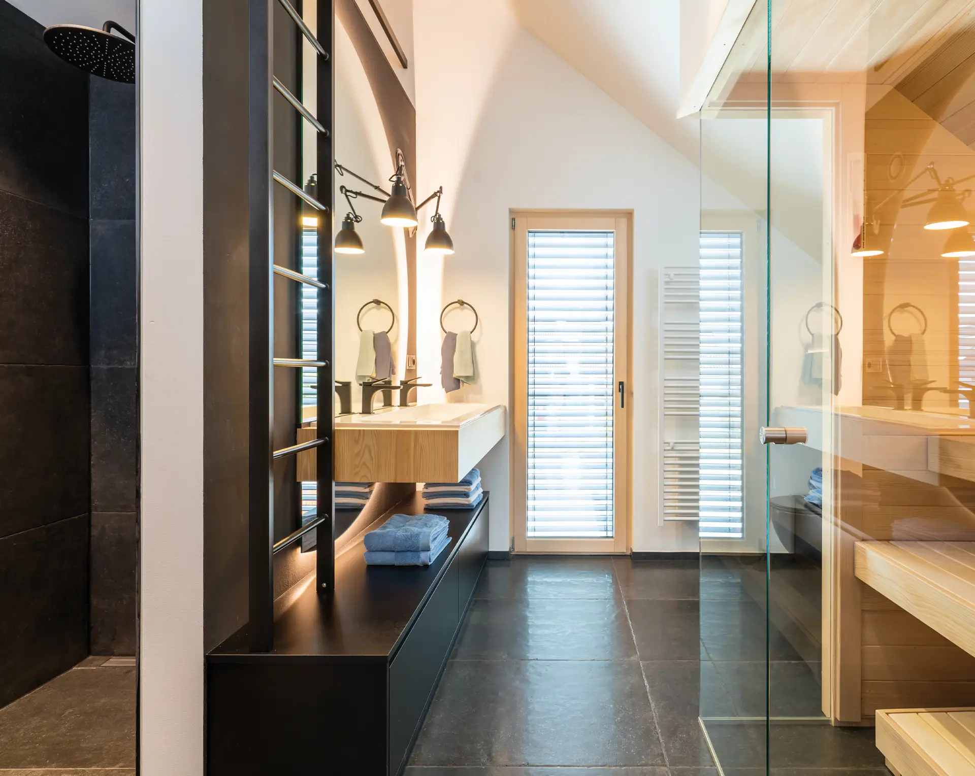 Modernes Badezimmer mit dunklen Fliesen, wandhängendem Waschtisch aus Holz und einer Ganzglassauna.