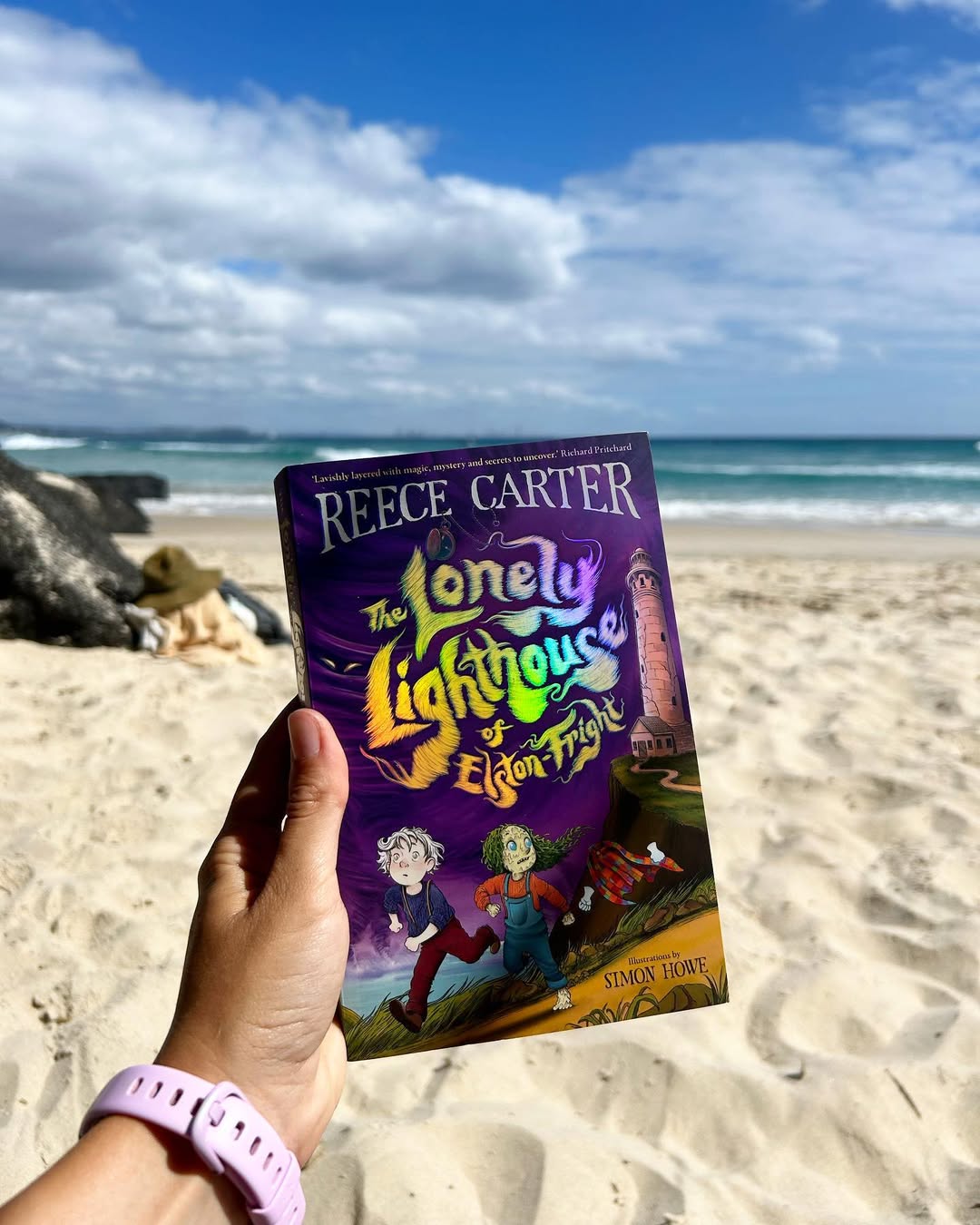 Erin Middleton holding a copy of The Lonely Lighthouse of Elston-Fright with the beach in the background.
