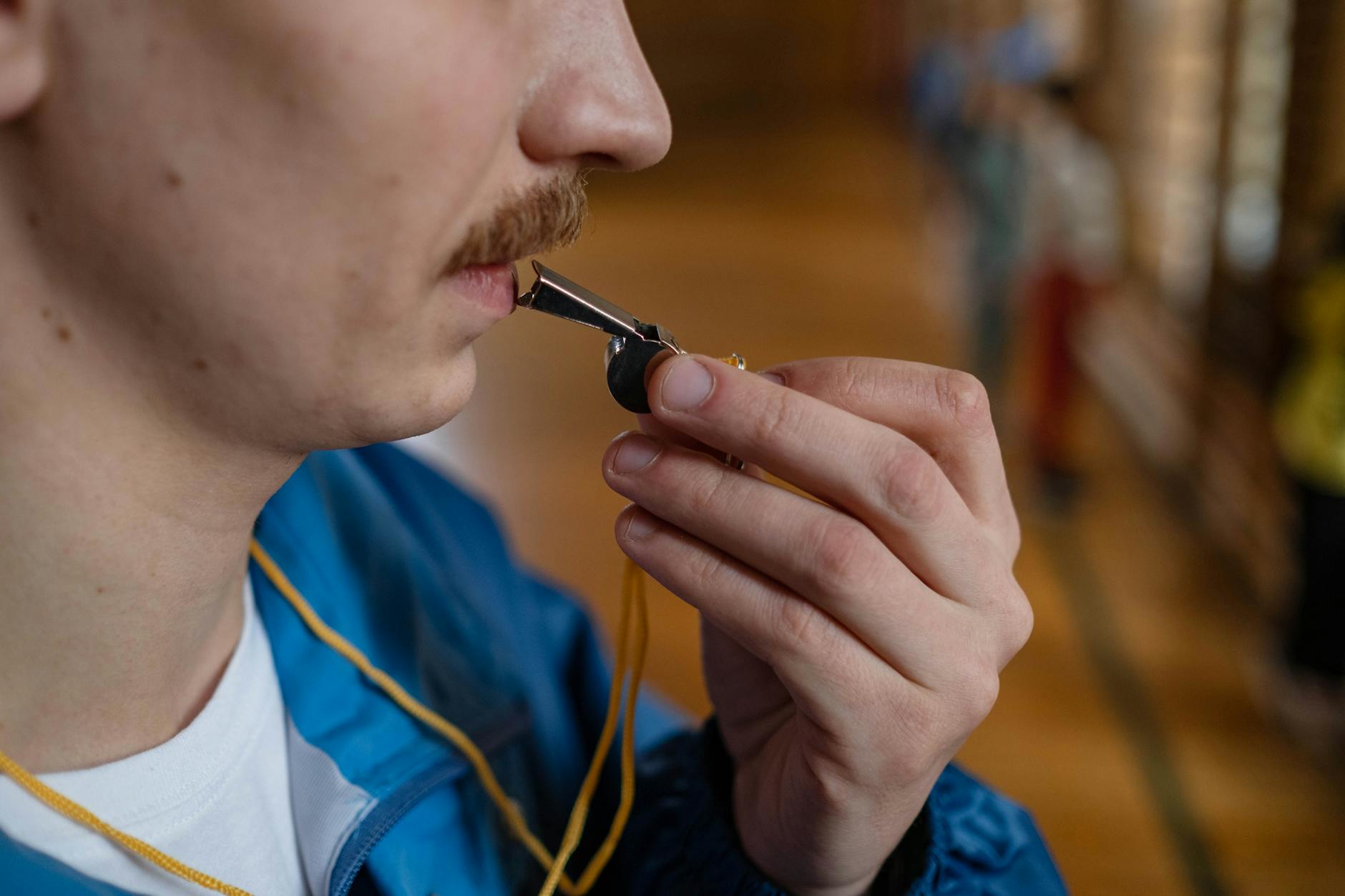 A teacher holding a tablet and whistle while standing on a bright blue gymnasium floor during a busy school day.