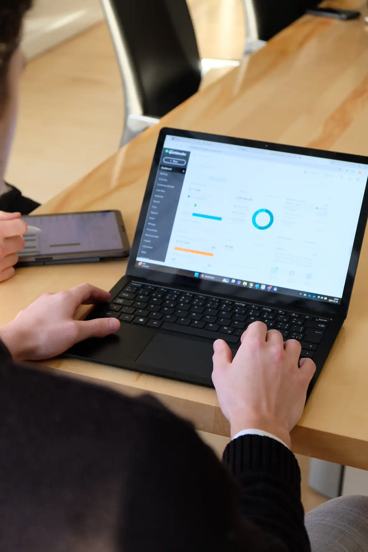 Vue en contre-plongée par-dessus l'épaule d'un professionnel analysant le tableau de bord financier de QuickBooks sur son ordinateur portable lors d'une séance de travail.