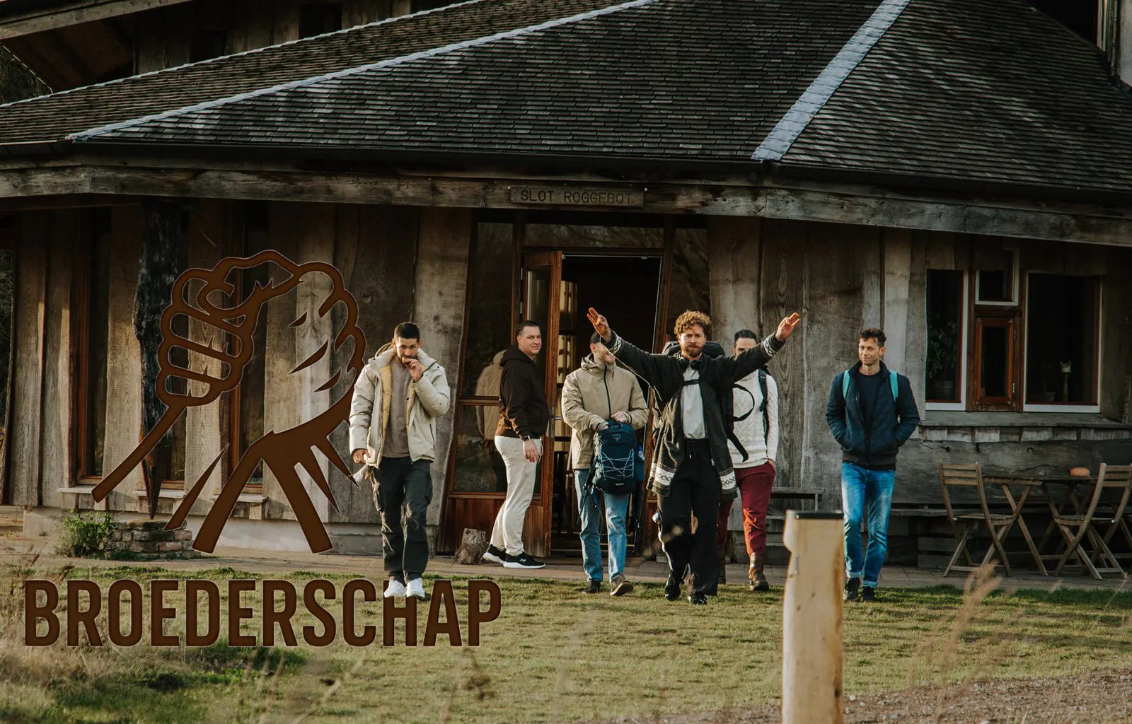 Een groep mannen loopt over het gras voor een houten gebouw, links het logo met twee handen en de tekst BROEDERSCHAP