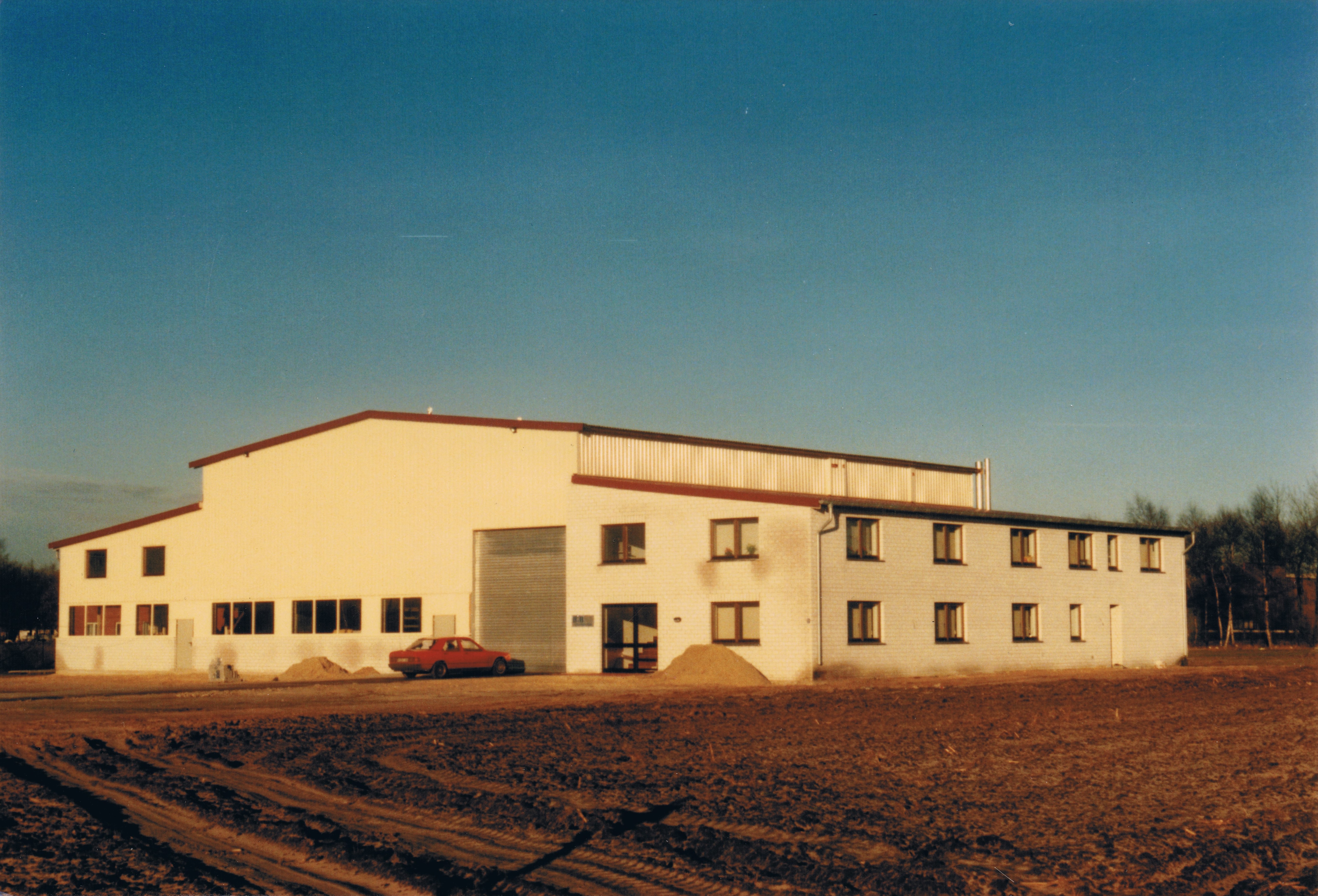 Großes Industriegebäude mit PKW vor der Tür, sonniger Tag
