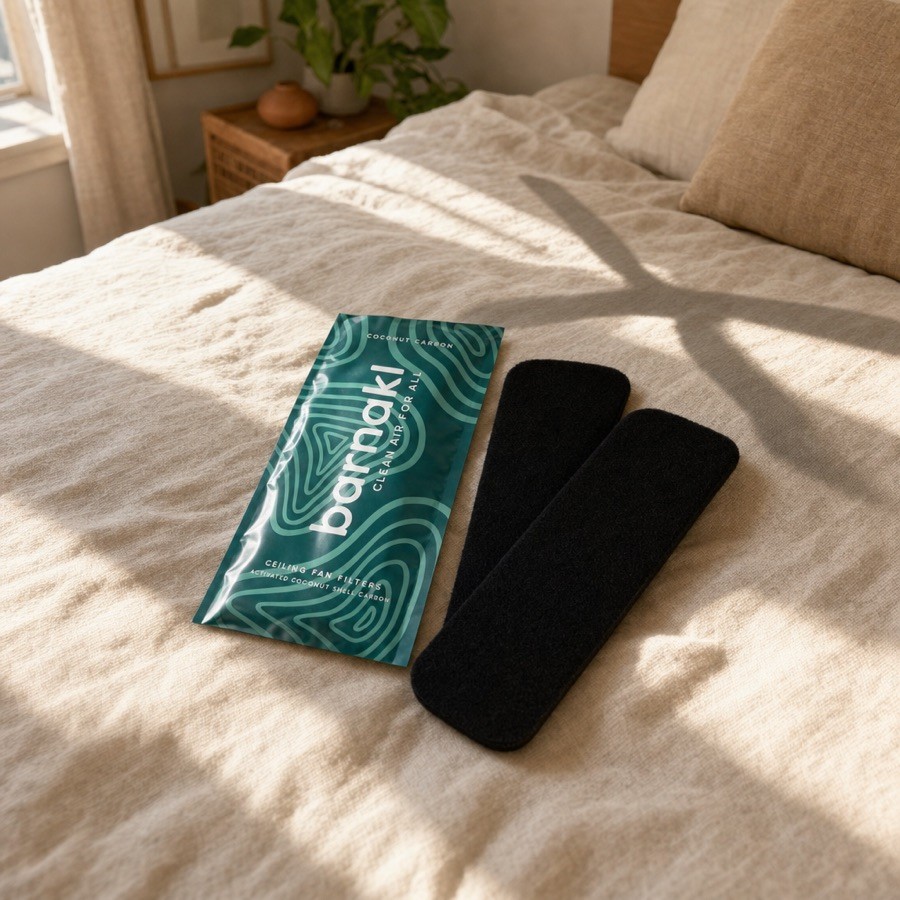 A teal Barnakl pack and two black carbon pads staged on a sunlit bed with a ceiling-fan shadow across the sheets