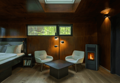 Cozy interior of a modern room featuring two chairs, a wooden table, and a small fireplace, with natural light.