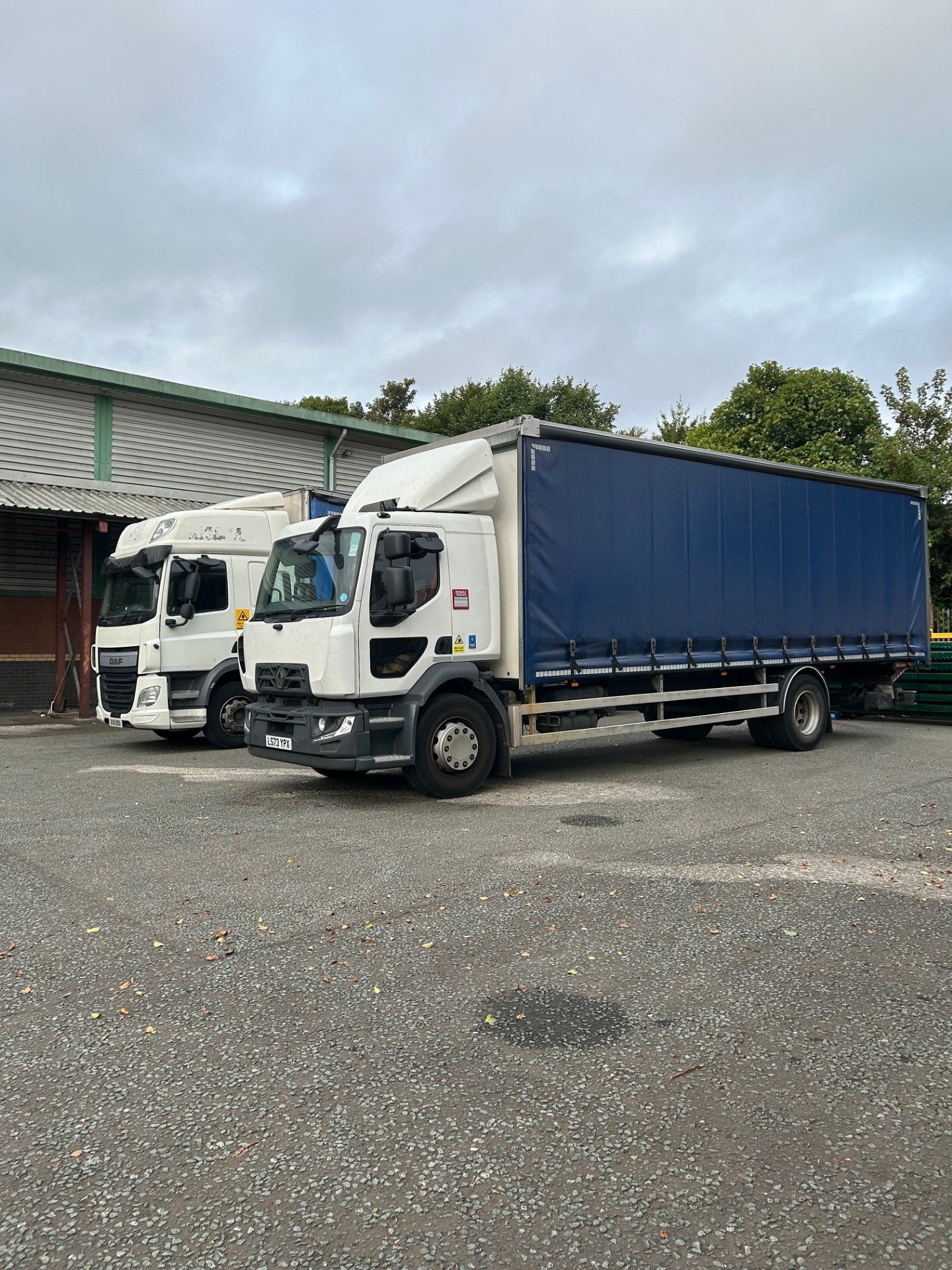 Image of two large haulage trucks parked in a warehouse yard