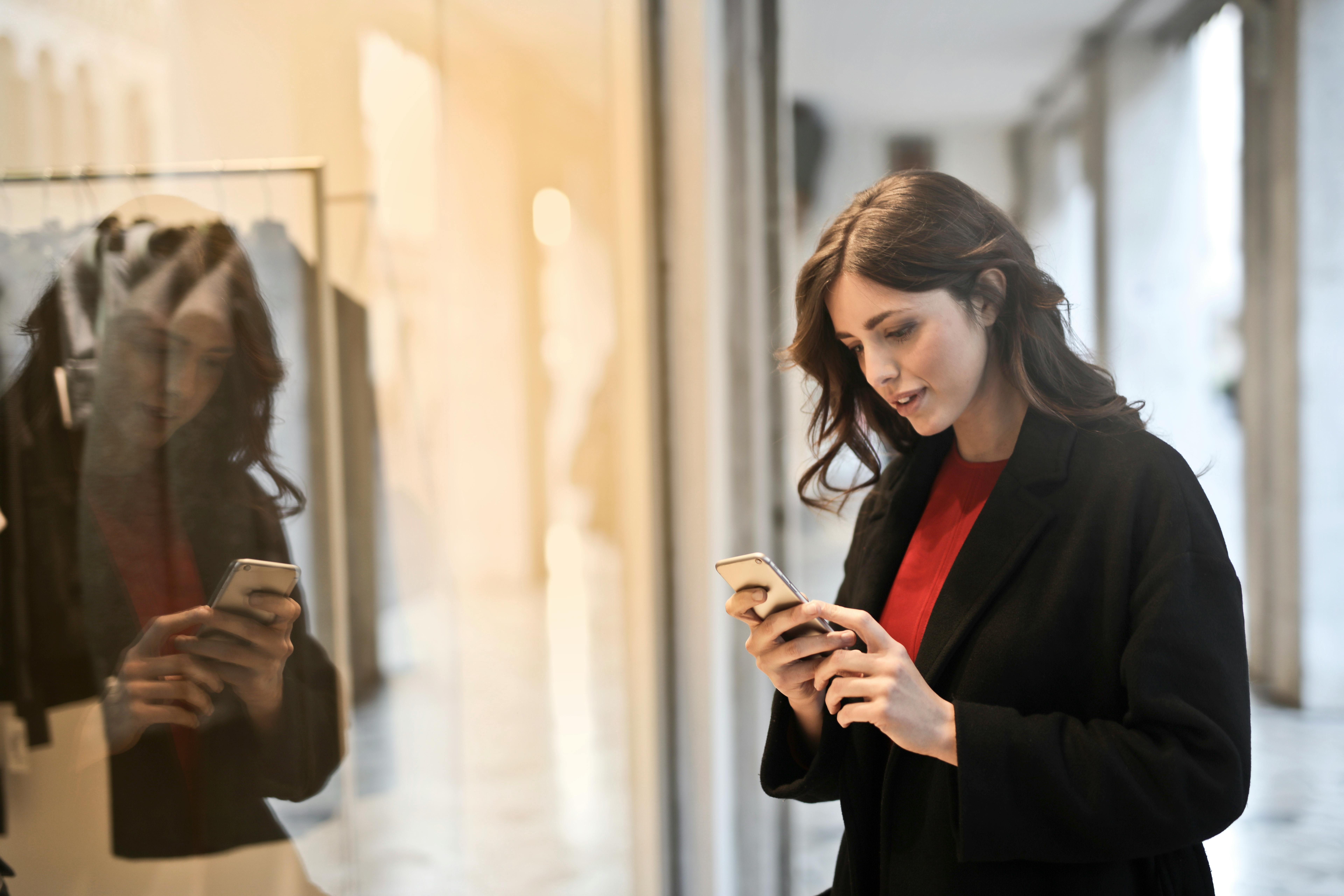 Woman checking rewards on her smartphone while standing outside a retail store.