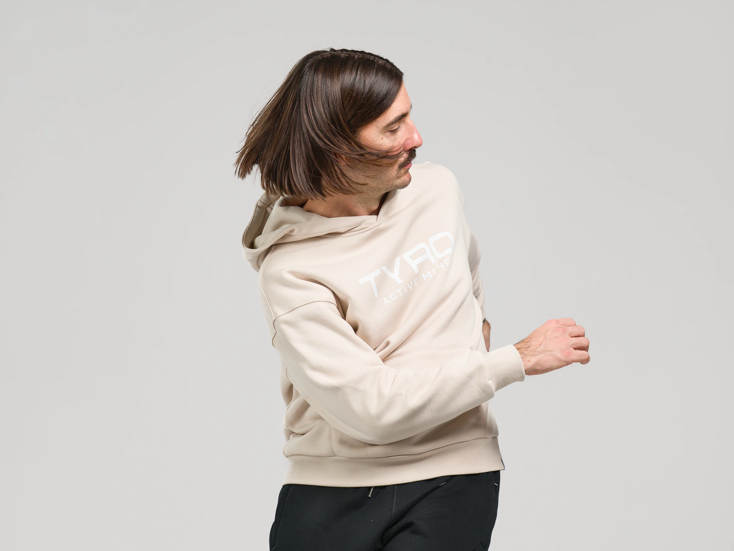 Person wearing a beige hoodie captured in a dynamic motion pose in a studio setting.