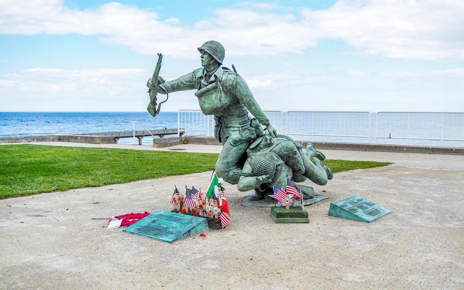 Statue of soldiers at Normandy D-Day Beach with flags and memorial plaques.