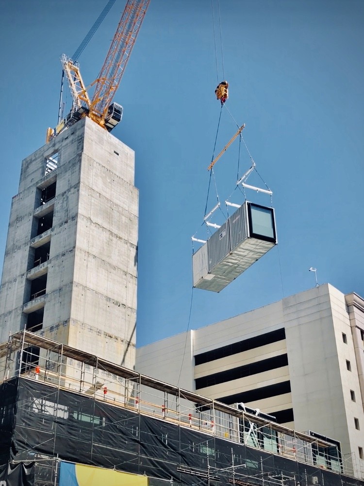 A glimpse into the next case study featuring a building module being expertly lifted by a crane and placed onto a concrete podium.