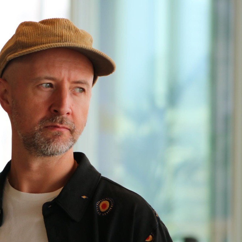 Smiling person with curly hair, wearing a black shirt, against a warm, dark background.