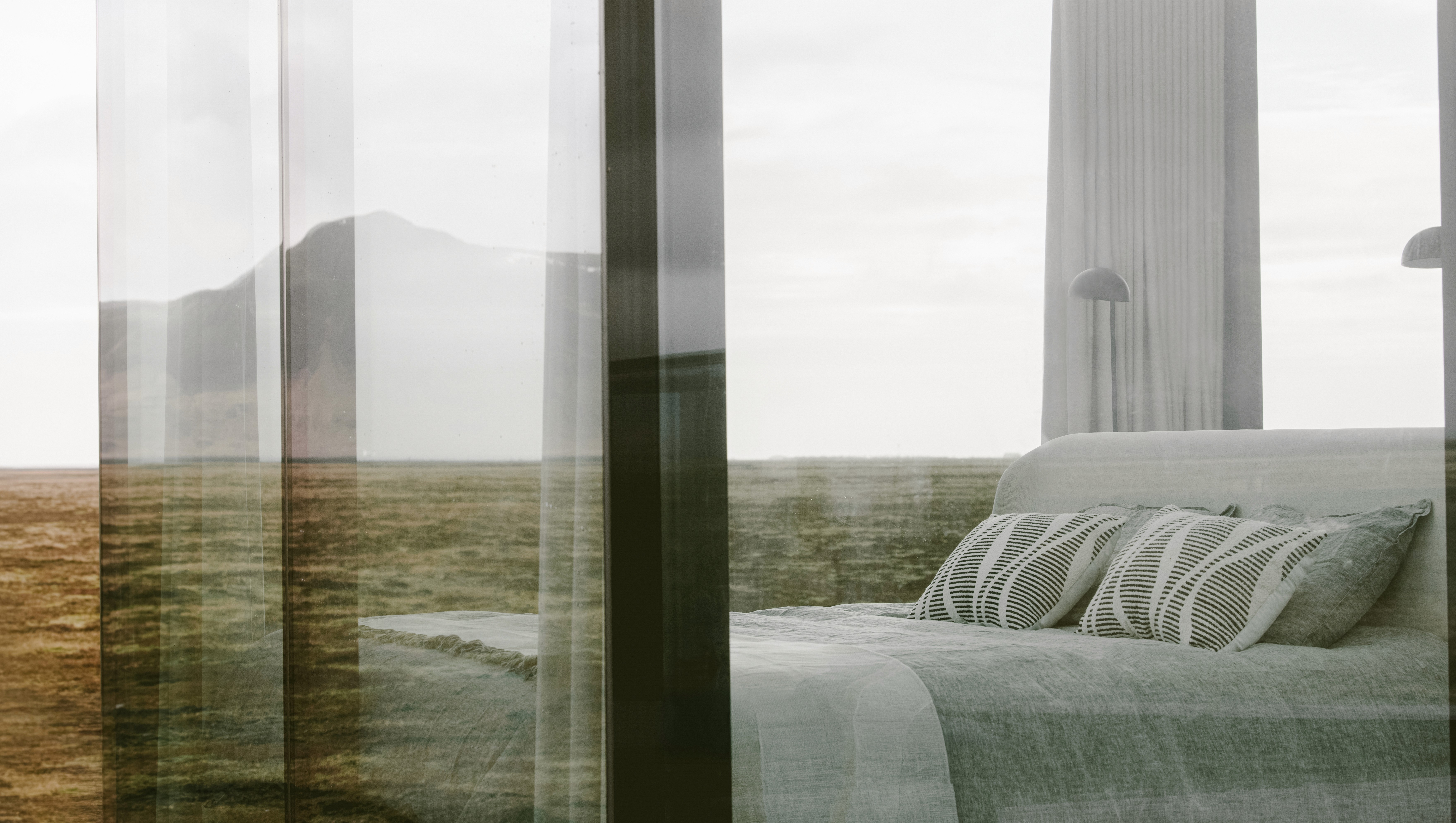 Minimalist bedroom with floor-to-ceiling glass walls and soft neutral bedding, overlooking a vast open landscape, designed as a modern luxury cabin retreat immersed in nature.