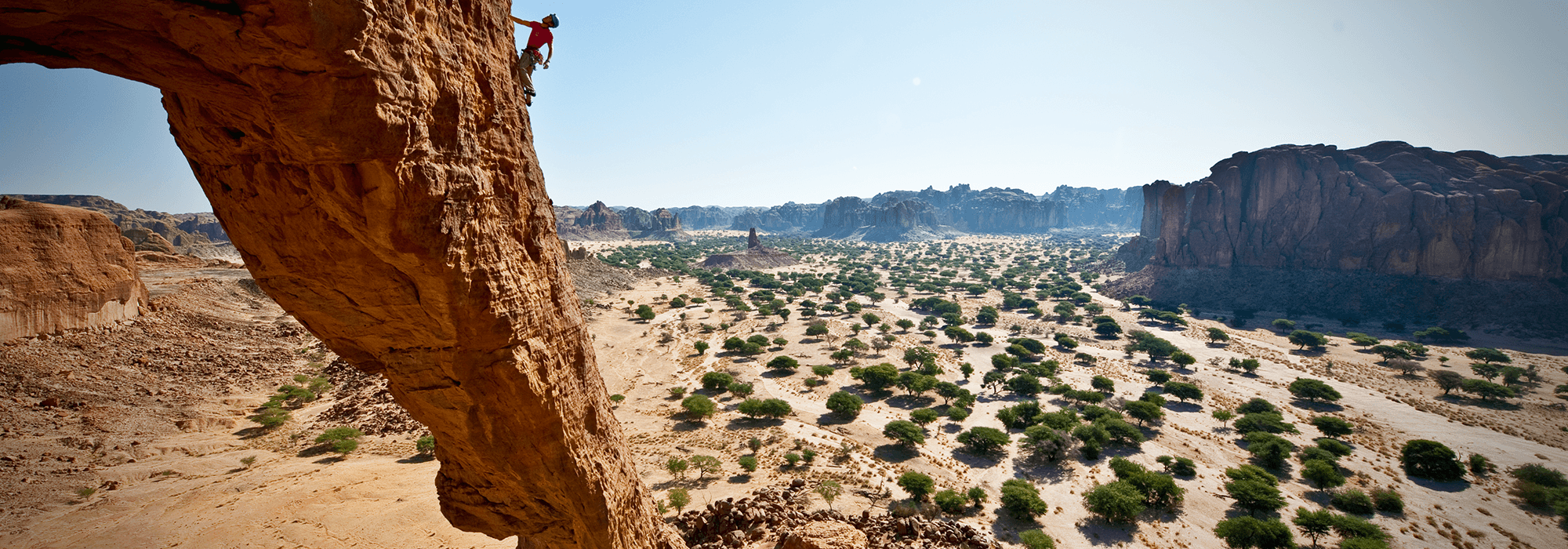 A climber pauses on a rock face to visualize their route on a unique rock formation in the country of Chad in northern Africa.