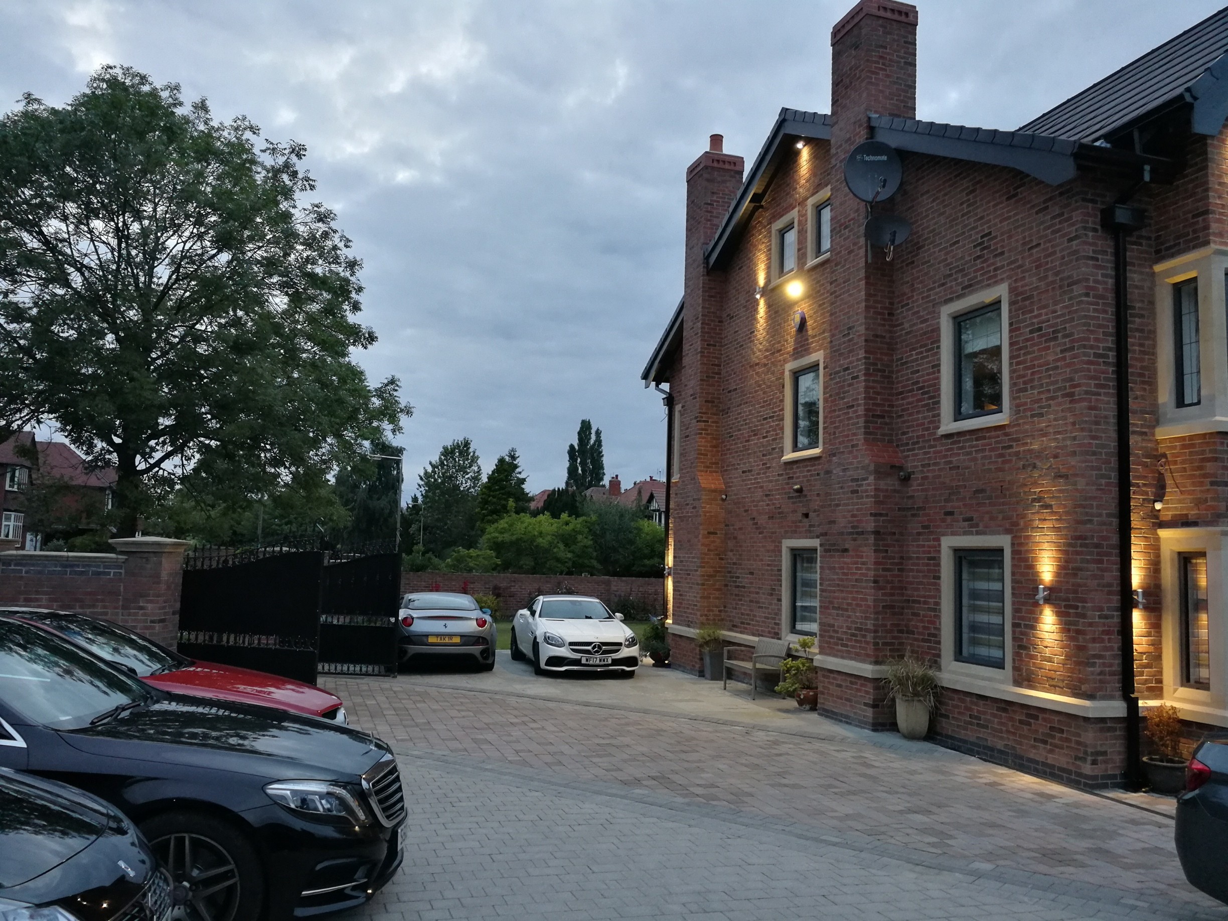 Side elevation of a remodelled luxury family home with brick façade, feature lighting, and landscaped driveway.