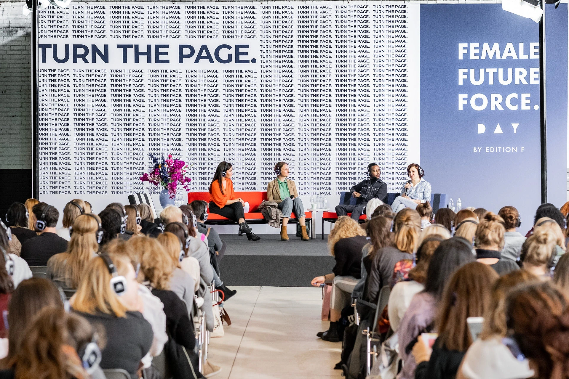 Panel talk on the Female Future Force Day stage in front of a wall covered in repeating Turn The Page lettering.