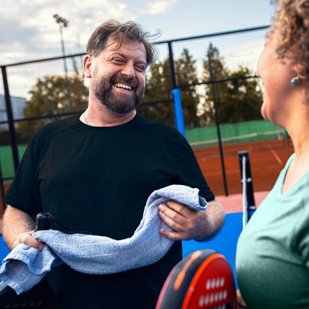 A smiling man holds a towel on a tennis court,.