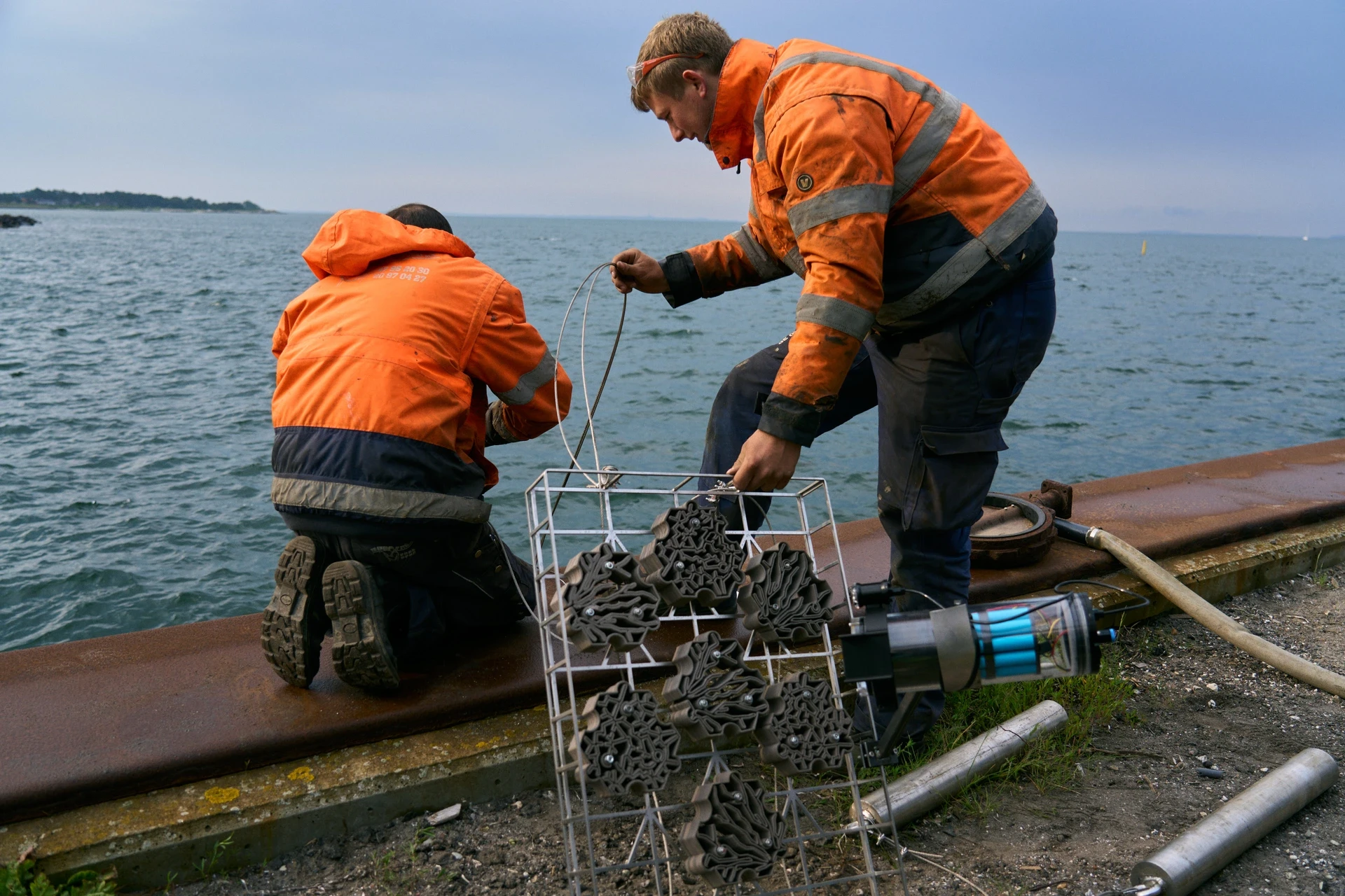 2 Workers in install a modular artificial reef structure with an underwater camera system AnemoCam along a coastal edge.