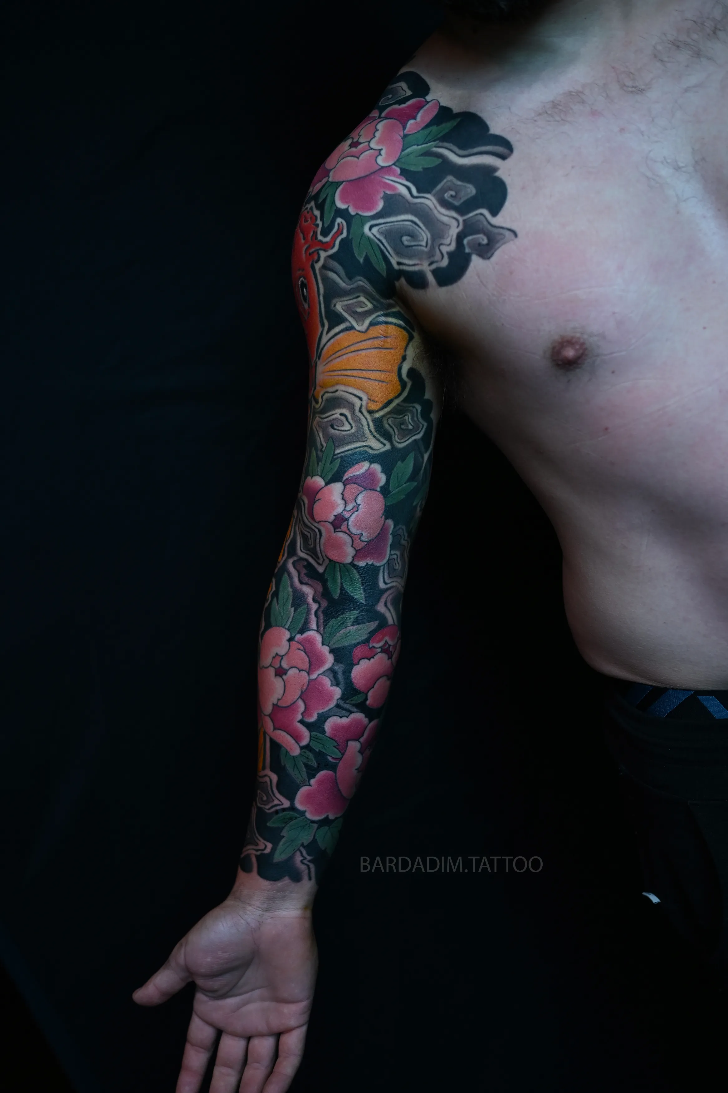 Inner side of the sleeve with the palm turned out, pink peonies descending the inner arm through grey carved waves to the wrist.