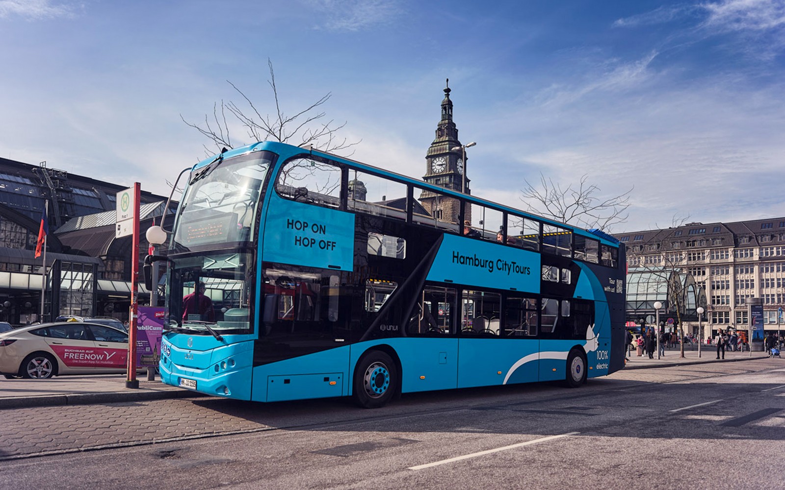 Hop-on hop-off bus in Hamburg city center near historic clock tower.