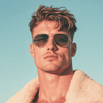 A man in aviator sunglasses and a fur jacket under a clear blue sky.